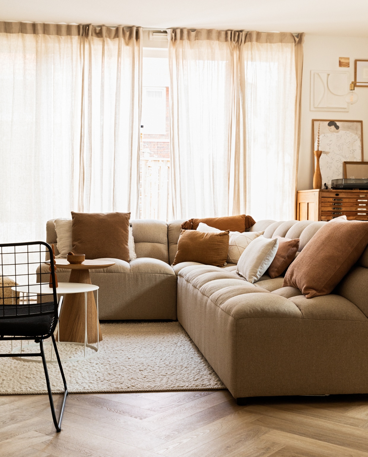 Bank Karwei, witte salontafel van k’willem in huis, houten bijzettafel Kwantum, kussens via Bij Emma Thuis en Mamoesjka, gordijnen Ikea, draaikaars op tafel Dille &amp; Kamille, vloerkleed en witte salontafel via Marktplaats, draadstoel Karwei, ladenkast Marktplaats, posters PSTR Studio, 3D-kunstwerk zelfgemaakt, klein houten kunstwerk Ruben van der Scheer, kandelaar van kringloopwinkel, wandlamp House Doctor, platenspeler Pro-Ject. vtwonen 09-2022 | styling Ilona Jongepier | fotografie Diana van Leeuwen