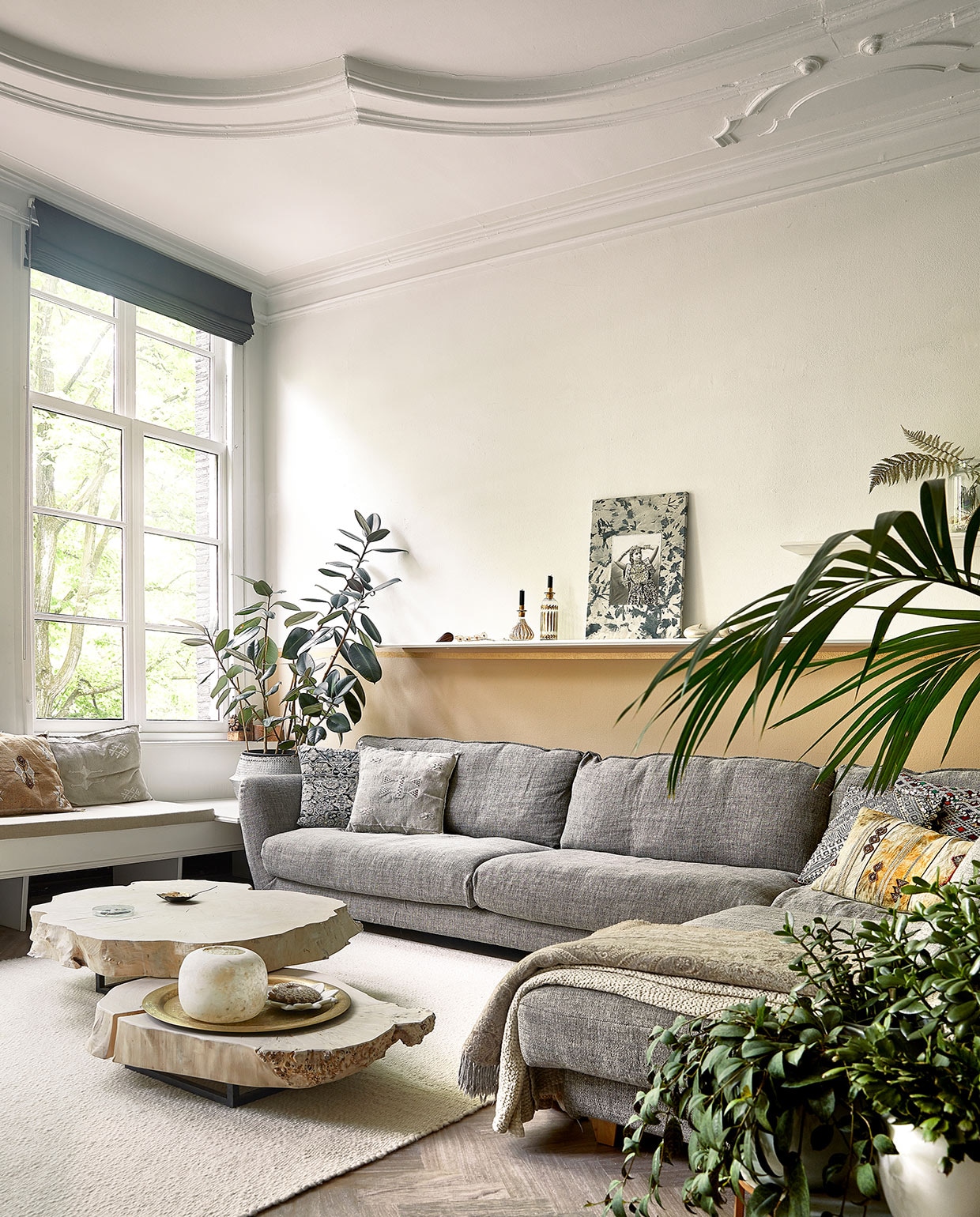 Raambekleding en vloer zaten al in het huis. Bank in vensterbank op maat gemaakt. Loungebank Seats. Kussens, plantenmand, tafels, plaid, kaarsenhouders/vazen, marmeren schaaltje en dienblad Zenza. Wollen vloerkleed Helsinki van Vloerkleden-winkel. Muurverf zelf gemengd. Bijzettafels Heerenhuis Manufactuur, fossiel van schelp, koperen schaaltje MaisonNL. Portret door dochter Naomi gezeefdrukt en geborduurd. vtwonen 06-2021 | productie Coco Features | styling Linda van der Ham | fotografie Peggy Janssen