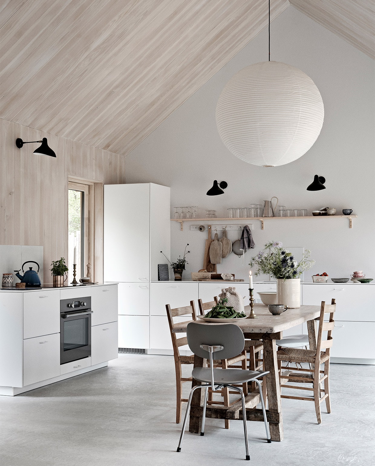 Keuken, wandrekken, glazen en hoge krijtwitte vaas Ikea. Eettafel en snijplanken Andrea Brugi. Metalen stoel Egon Eiermann, houten stoelen vintage. Vergelijkbare plafondlamp Lampion. Wandlampen Serge Mouille. Theeketel Le Creuset. Zilveren kan uit Griekenland, groen bord uit Marokko. Theedoek Aiayu. Overig onbekend. vtwonen binnenkijken special 03-2022 | productie Revolver, Living Inside | fotografie Mikkel Tjellesen | styling Marie Monrad Grounbøl