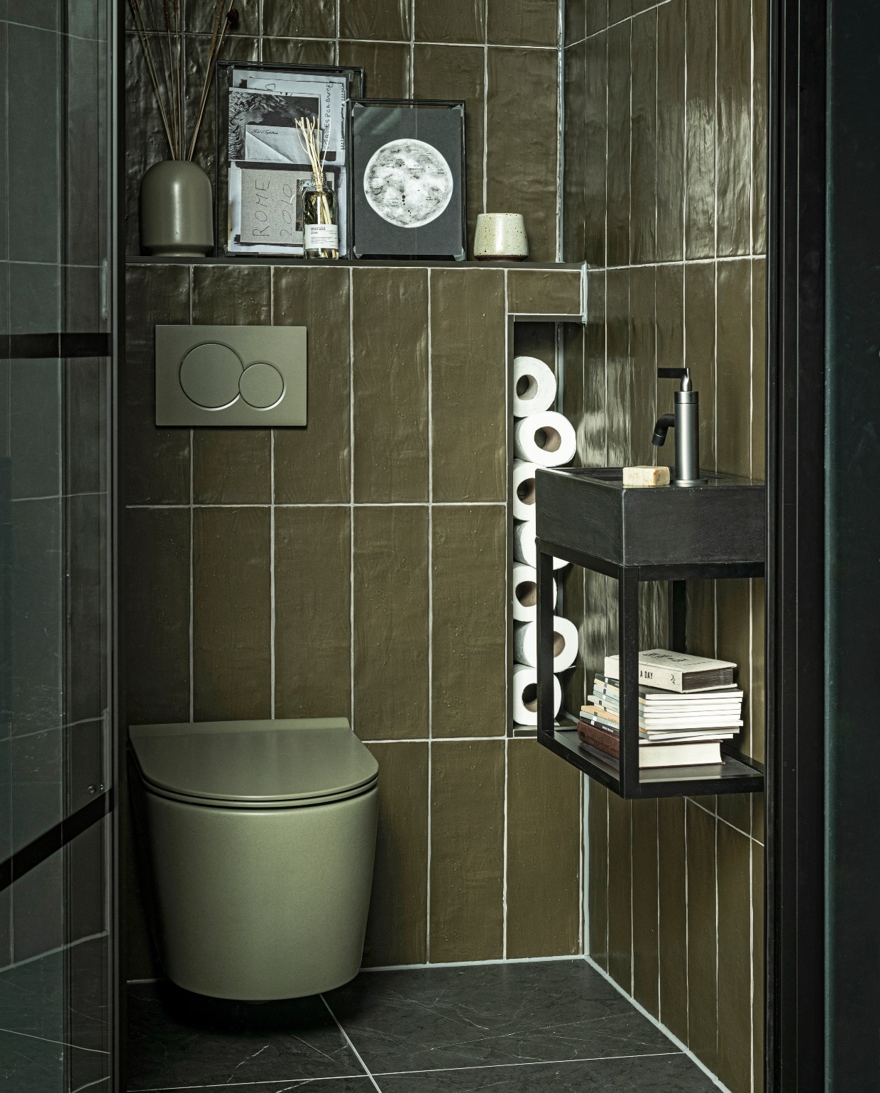Fontein Tank in kleur Concrete Black, 40x22x10 cm(bxdxh) € 299,- (ook in Concrete en in White, hoogte 5,5 cm), metalen onderstel Fontein Frame in Zwart, 40x22x30 cm (bxdxh) € 339,-, hendel wastafelkraan Grip in kleur Black Steel € 459,- (ook in Charcoal, Bronze,Brushed en Chrome en met twee hendels), wandtegelMediterranea in kleur mat Camouflage, 3,2×40 cmper m² € 61,75, vloertegel Classic Black mat, 74×74 cmper m² € 73,05 (ook in 74×148, 30×60 en 7,3×30 cm).M.m.v. tegeldepot (toilet), ikea.nl (vaas), vtwonen.nl (fotolijsten). vtwonen collectie 08-2020 badkamer | styling Kim van Rossenberg | fotografie Sjoerd Eickmans