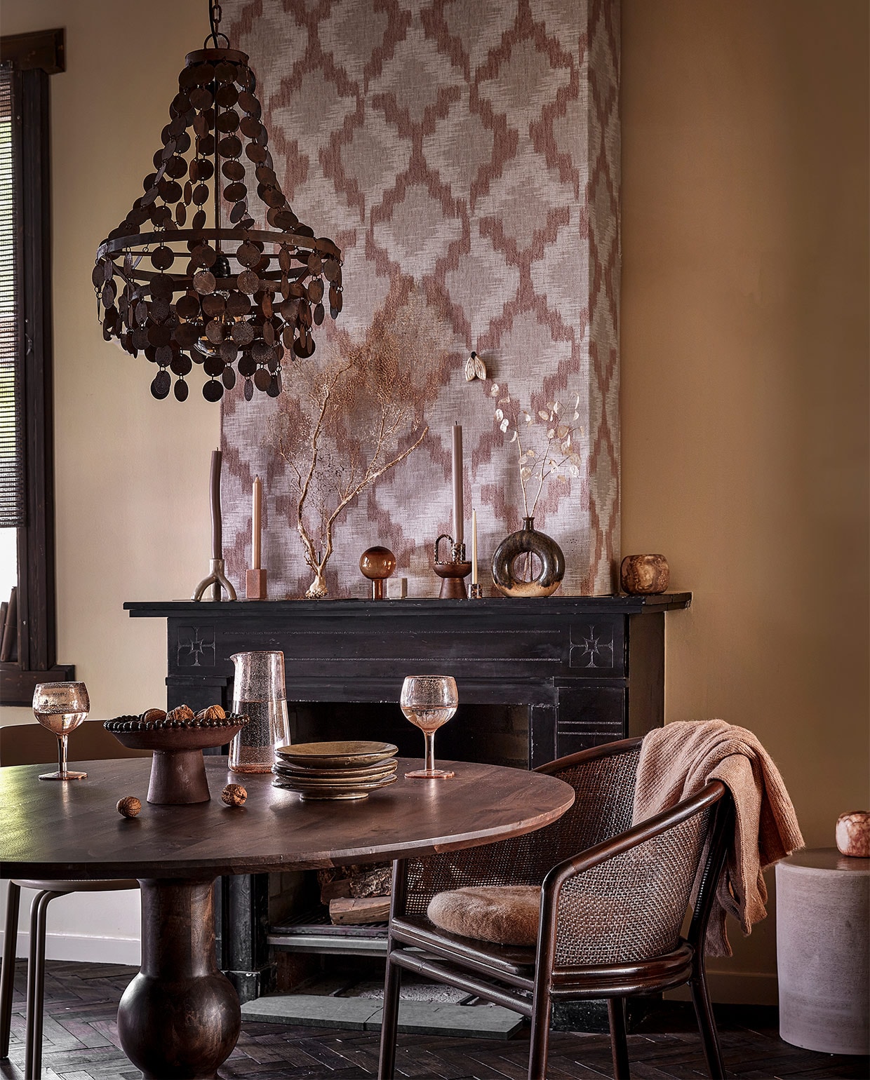 Behang Grounded Tribal 220603 van BN Walls, 100×53 cm € 37,95 (behangwereld.nl). IJzeren kroonluchter Balou, 29x29x55 cm (bxdxh) € 319,00 (hoffz.nl). Kandelaar met drie poten Brazilian Nights € 24,95, keramieken object vlinder € 10,95 (alagonda.nl). Roze natuurstenen kandelaar € 16,67, natuurstenen kandelaar blok € 15,15, donkerbruine eetkamerstoel, teakhout en rattan, 58×77 cm (bxh) € 814,40 (nordal.com). Gestreepte dinerkaars € 2,25, bruine kandelaar met hengsel € 6,95, glazen dop van karaf € 34,95 (vita32.nl). Houten kandelaar voor stompaars € 10,95, taupekleurige dinerkaars € 2,25, cirkelvaas € 33,95, roze windlicht € 59,95, gebreid vest € 59,99 (loftloft.nl). Minikandelaar € 6,50, minikaars € 0,45, bruin windlicht € 17,50, rond kussen € 16,50 (stijldepot73.nl). Droogbloemen (@tuinvanjudith). Beige eetkamerstoel Oda van Broste Copenhagen, 76x40x52 cm (hxbxd) € 577,25 (vtwonen.be). Eetkamertafel Blanco van BePureHome, mango- en walnoothout, 120×75 cm (Øxh) € 629,- (basiclabel.nl). Roze wijnglazen per stuk € 11,50, roze karaf € 21,75 (bungalow.dk). Bruine schaal op poot € 80,- (@studio.cherrymoon). Handgemaakte borden per stuk € 7,50 (@flowerchild.arnhem). Bijzettafel van Serax 32x32x29 cm (bxdxh) € 345,- (loods5.nl). Gebogen dinerkaars, object koraal en leren boeken in vensterbank privébezit. JA | vtwonen 10-2022 | styling Demelza Krens | fotografie Peggy Janssen