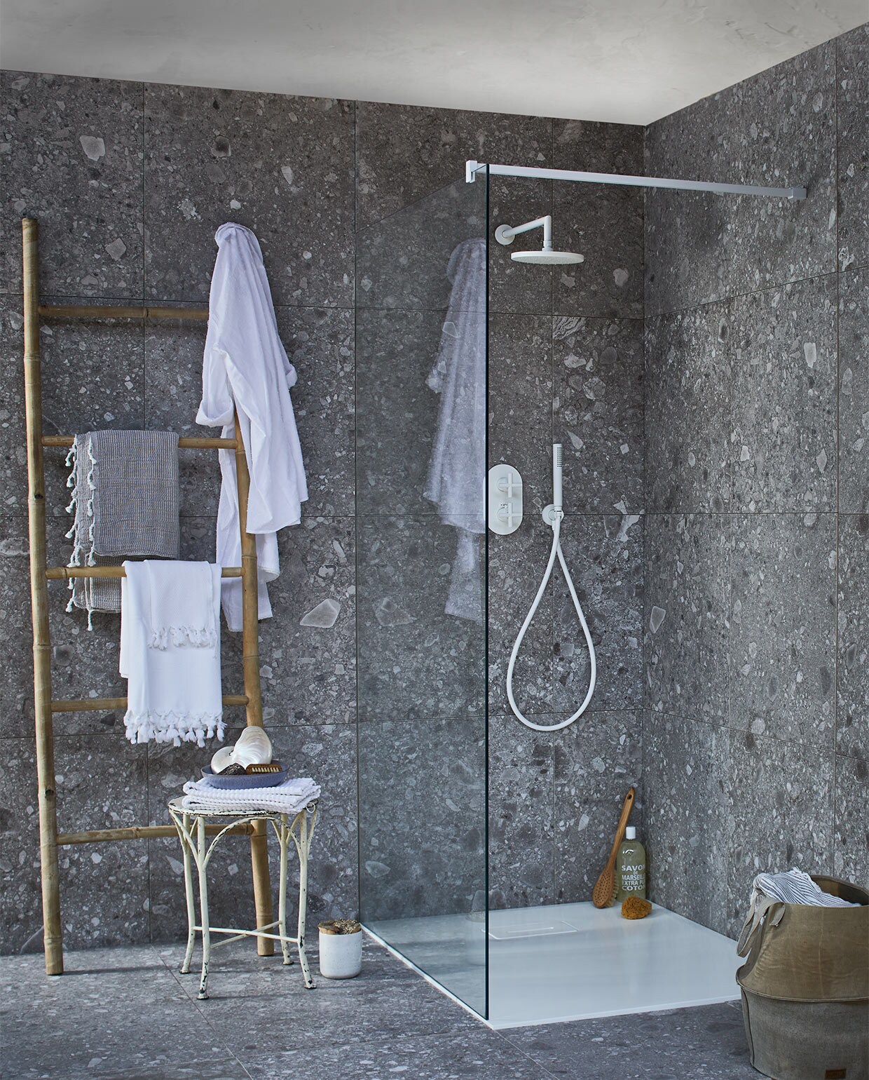 Op de wand en vloer: tegel Composite Dark Grey van vtwonen tegels by Douglas &amp; Jones, douchevloer met geïntegreerde afvoer van gegoten marmer in powder white, glazen douchewand met muurbevestiging in powder white, diverse uitvoeringen (transparant,donkergrijs en spiegelglas), douchekraan Cross, muur-versie powder white met afdekset voor inbouwthermostaat, handdouche, douchearm, hoofddouche. Bamboe ladder, witte badmat op kruk (l’Etoile Conceptstore). Hamamdoeken (Ottomania). Badborstel, nagelborstel (My Deer Store). Witte schaal (Raw Materials). Douchegel, spons (&amp;Klevering). Kruk (Neef Louis). Canvas mand (Hoffz). Schelp (De Weldaad). Pot met kurken deksel (Restored). JA | vtwonen 02-2017 | styling Cleo Scheulderman | fotografie Jeroen van der Spek | productie Inge Steketee