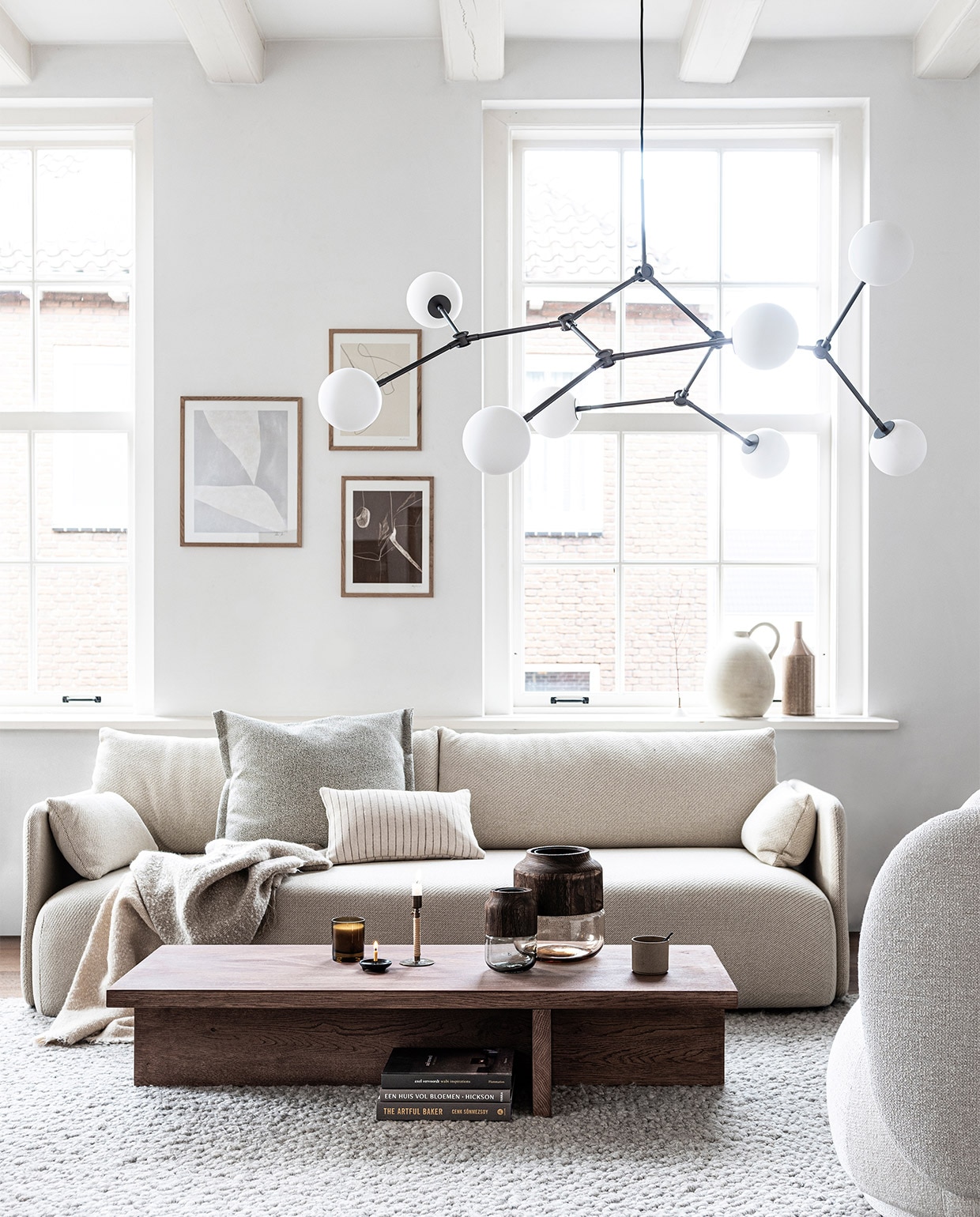 3-zitsbank Offset van Norm Architects in wit-beige stof Coda van Kvadrat, 224,3x90x65,6 cm (bxdxh), zithoogte 37 cm, grijs vloerkleed Gravel, 200×300 cm, kandelaar Duca messing met rotan (menu.as). Hanglamp Drop Chandelier Bulb, 155x120x91 cm (lxbxh) (101cph.com). Art prints: rechts boven Assembly Line van Anna Johansson, 30×40 cm, rechts onder Perspectives van Anne Johansson, 30×40 cm, eikenhouten lijst 30×40 cm, links Edge No. 04 van Hein Studio 40×50 cm, eikenhouten lijst 40×50 cm (theposterclub.com). Plaid 140×190 cm, beige kussen met bruine streep, 30×50 cm beige vaas met handvat geurkaars (zarahome.com). Kussen Plica van Hay, 55×60 cm, vazen met houten bovenkant Colletto van Leonardo, Ø 18 cm , Ø 25 cm , hazelnootkleurige vaas met tuit van Madam Stoltz, 14×40 cm (vtwonen.nl). Zwarte keramieken kaarsenstandaard (pantoufle-design.nl). Fauteuil Rico in off-white bouclé van Ferm Living (flinders.nl). Overig privébezit. vtwonen 01-2020 | styling Kim van Rossenberg | fotografie Sjoerd Eickmans