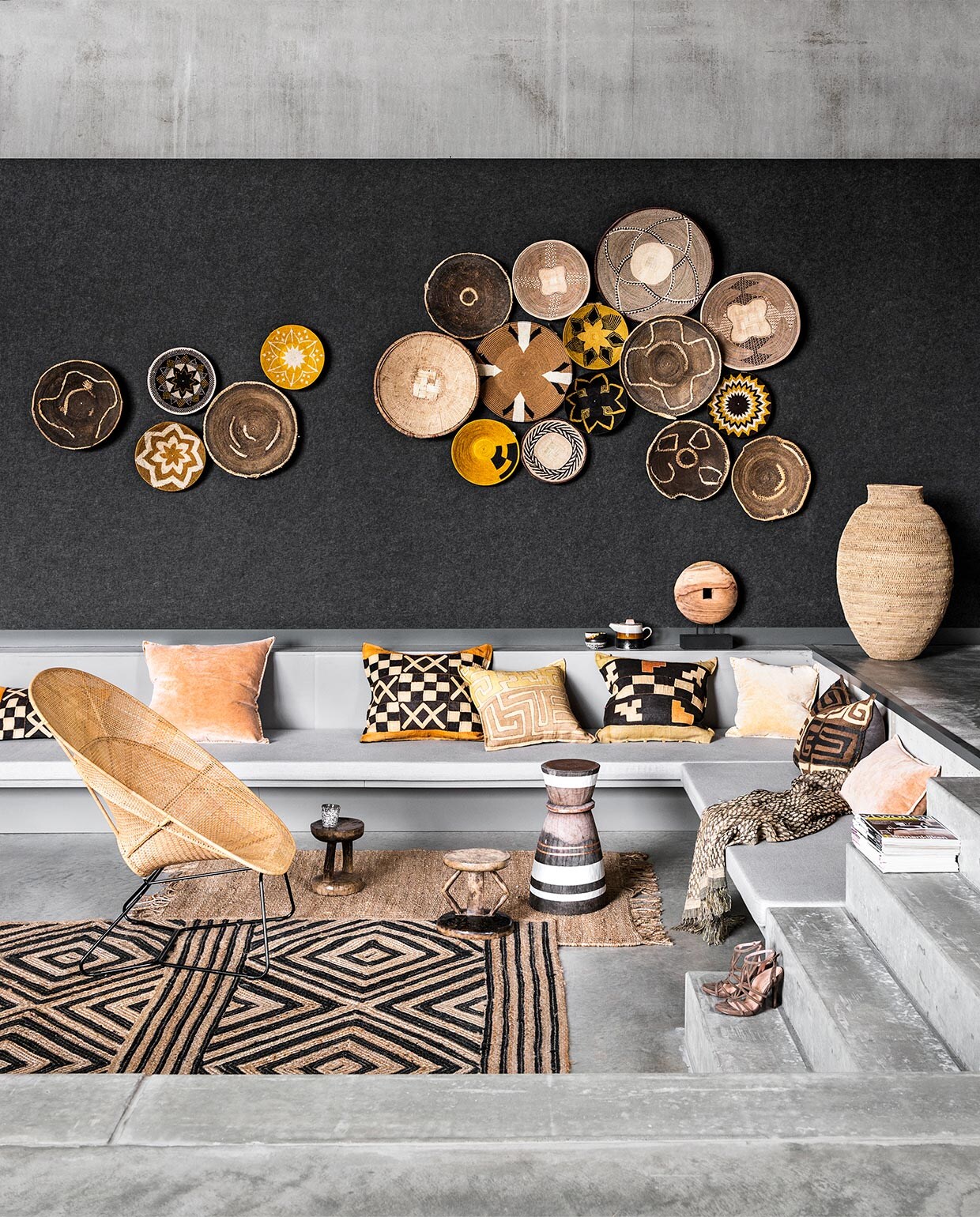 Triplexplaat bekleed met donkergrijs vilt (hollandfelt.nl). Gevlochten schalen van katoen en riet in diverse tinten uit Swaziland, vijzel omgedraaid in gebruik als tafeltje van de Tonga Tribe in Zimbabwe, Batonga krukjes uit Zimbabwe (Couleur Locale). Oude grof gevlochten Makenge schalen uit Zambia, donkerbruin met lichtbruin, in verfijnde patronen gevlochten Binga baskets, bruin/naturel, Buhera basket uit Zimbabwe (boxworx.nl). Vierkanten velours kussens, kussens met donzen vulling gemaakt van Kuba kleden, linnen/zijde plaid en jute vloerkleed met geometrisch patroon, 170×240 cm (ML Fabrics). Langwerpig velours kussen, ornament van hout op voet, theepot, kommetjes, mok, vloerkleed jute naturel (HK Living). Rieten stoel (Pols Potten). Schoenen (Tamaris). vtwonen 02-2018 | styling Marianne Luning | fotografie Stan Koolen