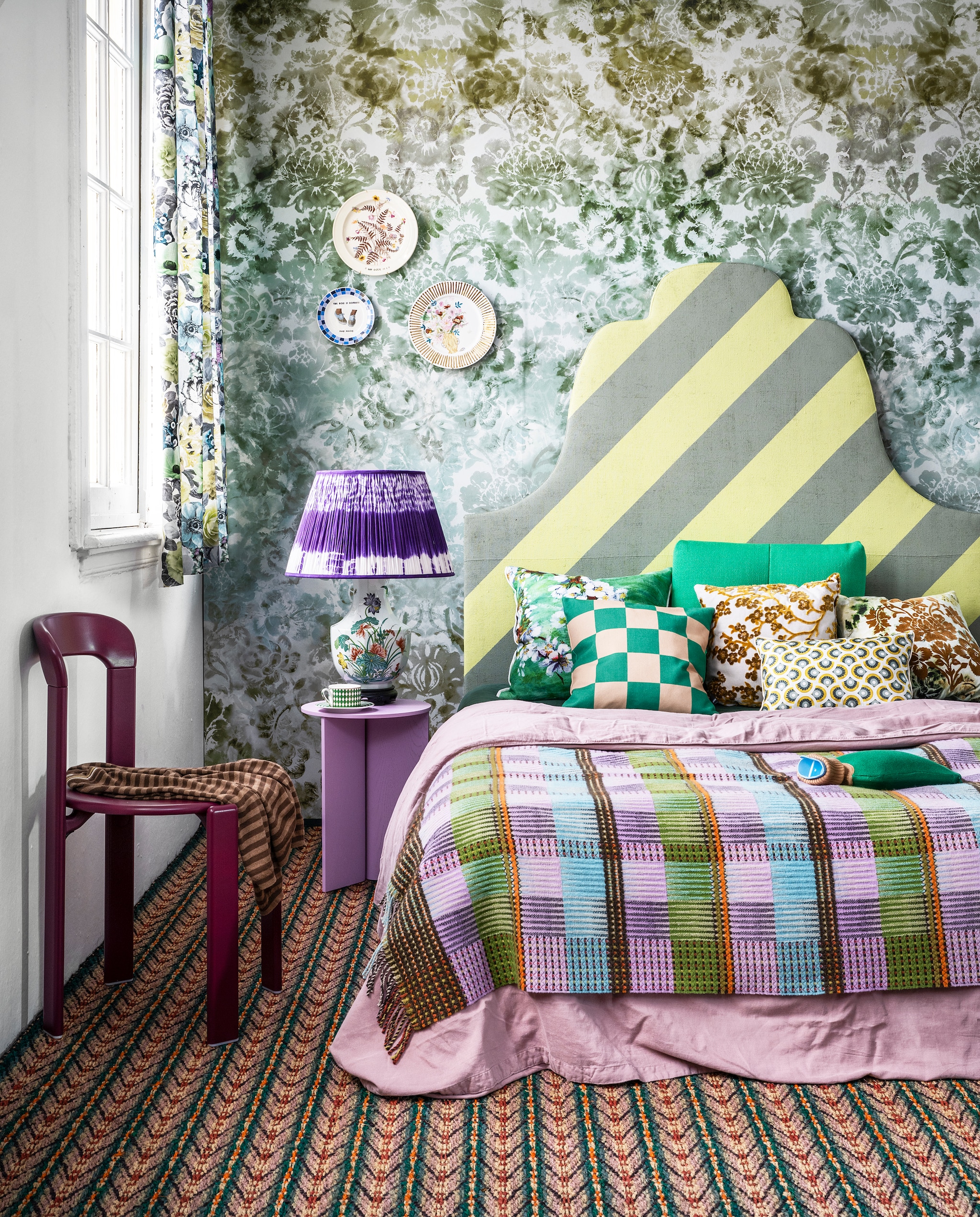 Behang Tarbana Damask van Designers Guild, 140×300 cm € 312,-, gebloemde gordijnstof Oriana van Designers Guild, 140 cm breed € 118,- (wva.nl). Gestreepte kokos vloerbedekking nr. 9022, per m2 € 97,- (cunera.nl). Bedhoofdeind van Combitex met groen-gele diagonaal geverfde strepen, prijs op aanvraag (com-anders.nl). Lila tafel van hout en staal € 215,-, stoel Rey in Grape Red € 559,-, groen rugkussen Quilton € 180,- (hay.nl). Roze linnen dekbedovertrek, 140×220 cm € 109,-, kruik € 39,95 (suite702.com). Geruite wollen plaid € 182,-, groen bloemenkussen, 60×60 cm € 174,-, bruin velours gedecoreerd kussen rechts Designers Guild € 131,- (wva.nl). Groen-naturel geruit kussen € 39,- (festamsterdam.nl). Velours kussen met Japanse bloesem van Zuiver € 40,50, kop-en-schotel van Pols Potten, per 4 € 145,- (vtwonen.nl). Vierkant zijden kussen van Lelievre € 89,- (loggerewillpower.com). Paarse tie dye lampenkap uit de Tribal collection van Vaughan Designs € 343,- (wva.nl). Gebloemde vintage lampenvoet € 85,- (hetgroteavontuur.nl). Vintage borden gedecoreerd door Lot Moorrees vanaf € 65,- (polspotten.nl). Kleding (vintagebrands.eu). JA | vtwonen 06-2022 | styling Marianne Luning | fotografie Stan Koolen