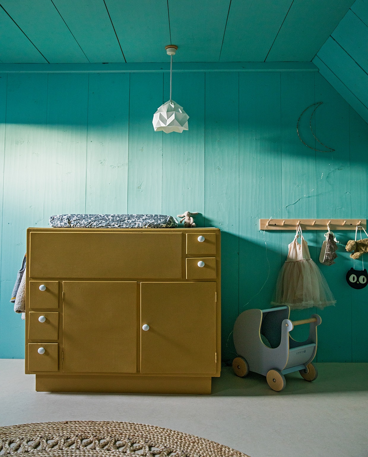 Muurverf Geest van Histor. Marmoleum-vloer Forbo. Commode gemaakt door de opa van Roos’ moeder, geschilderd in okergoud van Flexa. Hanglamp Studio Snowpuppe, kapstok Iris Hantverk, commodekussen Garbo &amp; Friends, poppenwagen antiek, vloerkleed Loods 5. JA | vtwonen 05-2021 | productie en styling Ilona Jongepier | fotografie Dana van Leeuwen