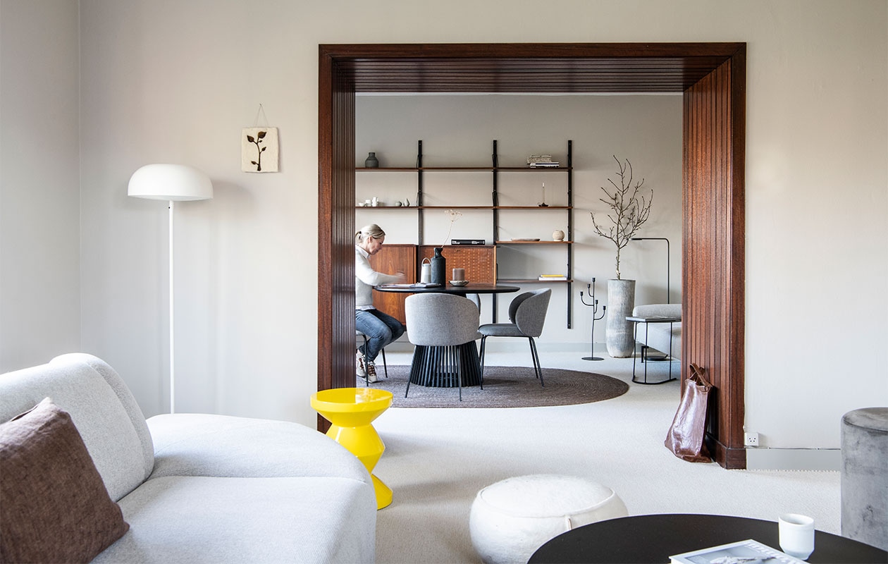 Muurverf Sikkens in RAL7044, mat. BankHKliving. Kussen Tell me more van Jet At Home. Witte poef Jacobien Life &amp; Style. Salontafel K’willeminhuis, stenen bakje en kaars Anne-Marie Wonen. Kunstwerkje Tiny Stories. Witte en zwarte vloerlampen Ikea. Gele kruk Zig Zag van Pols Potten.Zwarte eettafel Goossens Wonen. Zwarte vaas vtwonen. Muziekbox Bose. Stoelen Svenlars. Vloerkleed House Doctor. Vintage wandrek Meubelfabriek LOV Oosterbeek. In wandrek, van links naar rechts en boven naar beneden: vaas Urban Nature Culture, gerafeld notitieboek Lamali Paris Paper Booklet van Nomad Paulette, witte vazen Studio Peetlein, grijze vazen Lindform via Anne-Marie Wonen, boek Peter Lindbergh, ovale, marmeren schaal en witte vaas Anne-Marie Wonen.Kandelaar en bijzettafel K’willeminhuis. Tas Bea Mombaers for Serax via So Pure Store. Overig onbekend. vtwonen 07-2022 | productie Insidehomepage | styling Esther Loonstijn | fotografie LouisLemaire