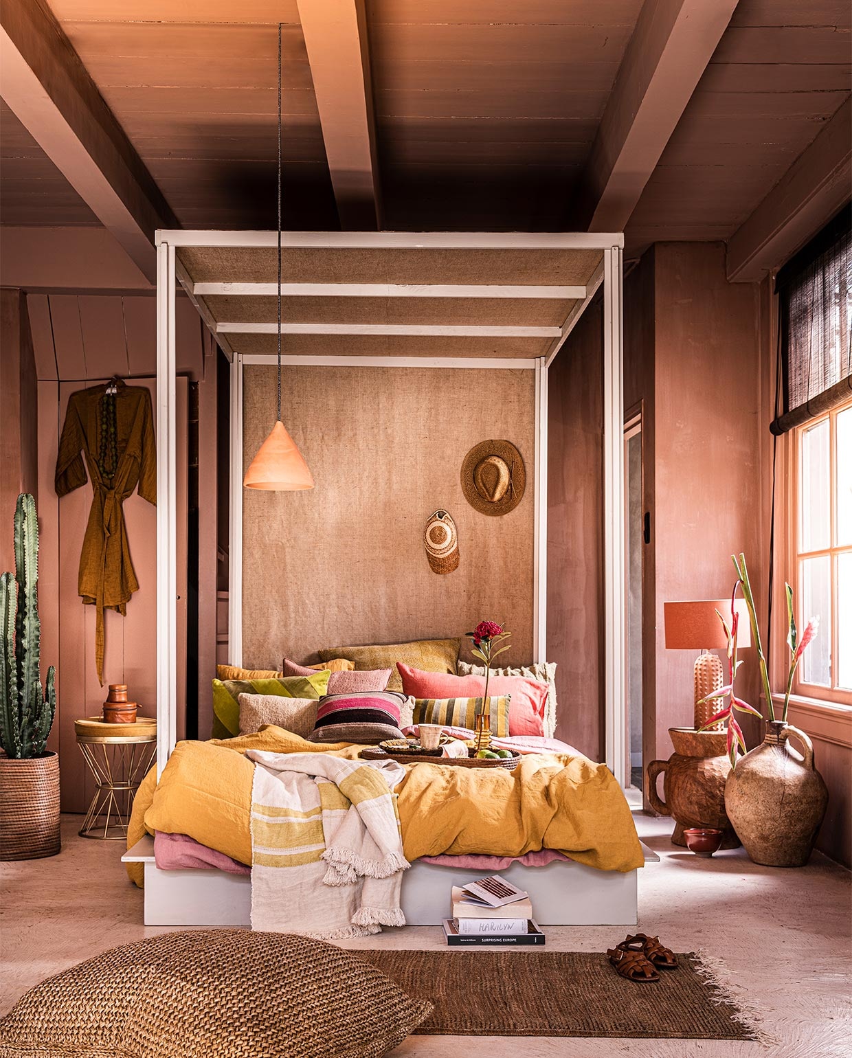 Verfkleur op wand Cypria van Carte Colori, 2,5 liter € 136,80, plafondlamp Maron, prijs op aanvraag, goudkleurige wand metallic stuc via Estudio, prijs op aanvraag, raambekleding Indivipro, prijs op aanvraag, bord Wonki Ware € 23,-, mok Wonki Ware € 19,- (brechtmurreatelier.nl). Handgemaakt hemelbed, prijs op aanvraag (com-anders.nl). Roze kussen met bruine streep € 125,-, roze kussen links daarboven € 163,- geel en roze linnen kussens, onderdeel van dekbed, per stuk € 39,-, geel en roze linnen dekbedovertrekken, per stuk € 325,-, langwerpig lichtgeel kussen € 215,-, dienblad, onderdeel van bijzettafel € 275,-, pet € 59,-, vaas € 1260,-, mand waar cactus in zit, onderdeel van salontafel € 275,-, kralenketting € 119,-, plaid met gele streep € 115,-, vloerkleed, 150x78 cm € 245,-, poef, 80x60 cm € 495,-, kussen met streepmotief achteraan € 249,-(couleurlocale.eu). Bruine glazen vaas Balloon van Normann Copenhagen, 19x7 cm (hxØ) € 36,80, rood schaaltje Merci van Serax, 15 cm € 21,40, groen langwerpig gestreept kussen van HKliving € 32,95, linnen servet van HKliving, set van 2 € 15,45, geel/groen kussen € 34,95 (vtwonen.be). Bloem in vaas en cactus, prijs op aanvraag (plantje.nl). Geel kussen met stiksels, 70x70 cm € 147,50, ochtendjas € 85,- (archive-store.nl). Hoed € 34,99 (koconceptstore.nl). Staande lamp € 119,- (sissy-boy.com). Houten kruk vanaf € 339,- (polspotten.nl). Hanglamp voor bed € 29,-, groene schaal € 16,- (householdhardware.nl). Sandalen € 59,99, set leren doosjes op tafeltje, vanaf € 29,99 (zarahome.com). Goudkleurig tafeltje € 169,-, onderste boek op stapel € 37,50 (maisonnl.com). Bovenste boek op stapel € 40,- (sukha.nl). Overige boeken privébezit. vtwonen 07-2021 | styling Liza Wassenaar | fotografie Sjoerd Eickmans
