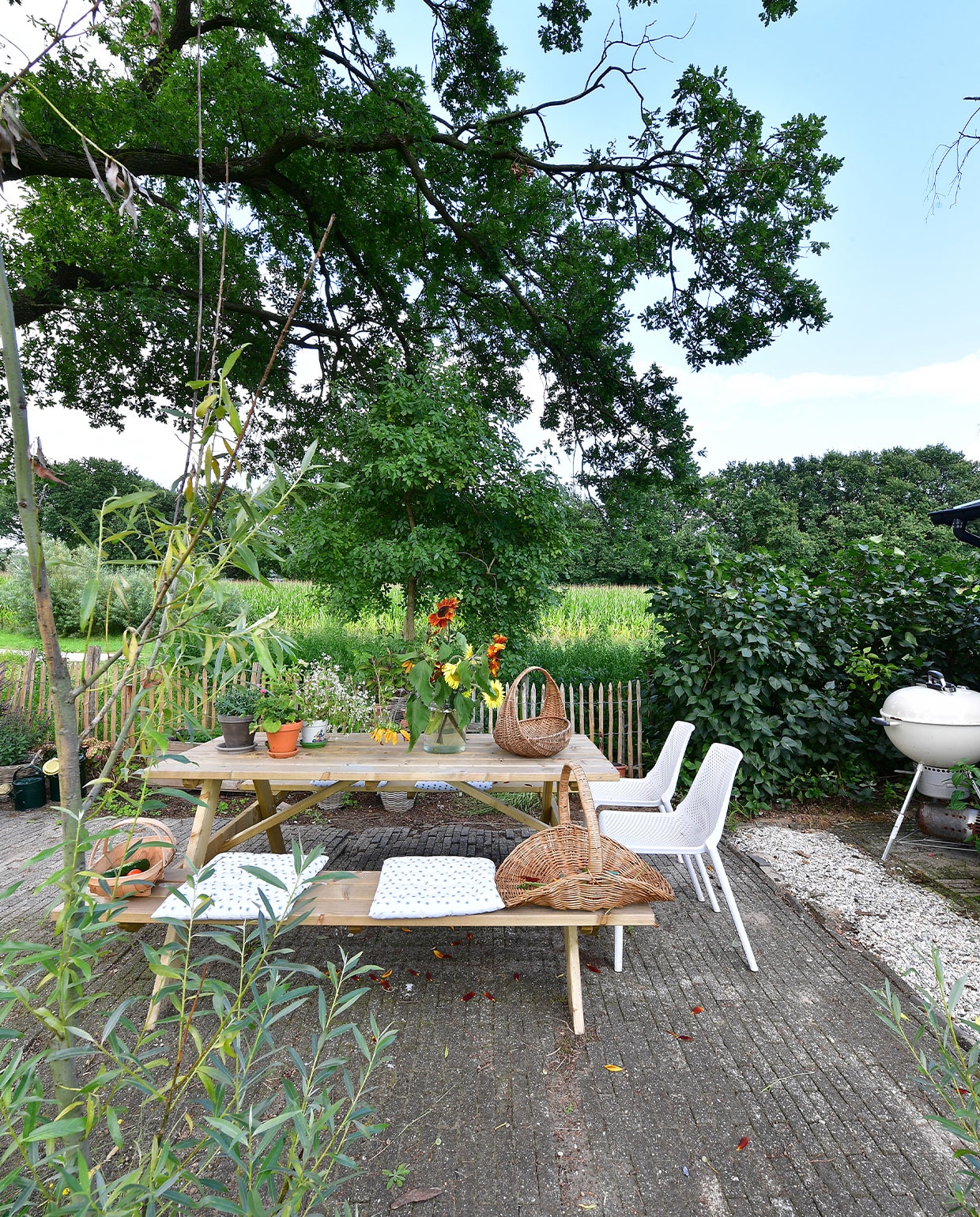 Strategisch ingericht in de schaduw van een eik: het terras. Een lekkere plek om te eten, maar ook om de plukboeketten te maken. Picknicktafel Karwei, barbecue Weber, stoelen gekregen, plukmanden kringloopwinkel, kussens Søstrene Grene. vtwonen tuin special 5 | fotografie Sietske de Vries