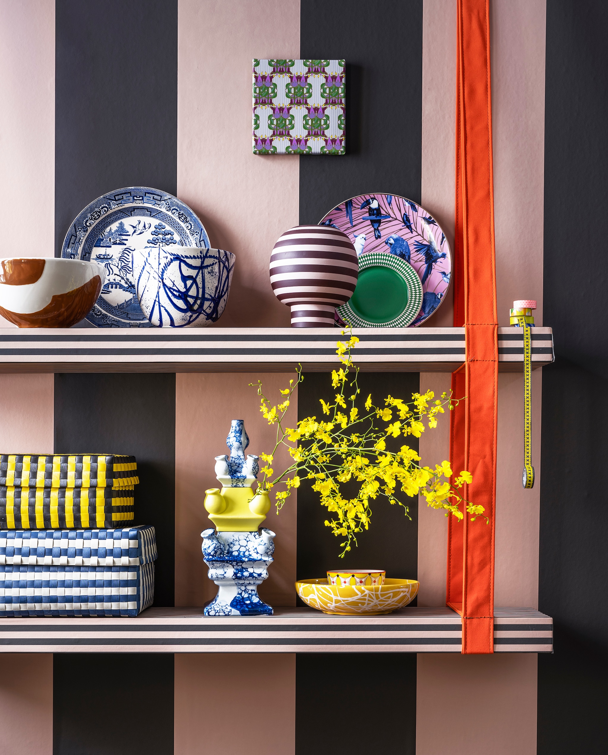 Planken met ophangsysteem van oranje band van Combitex, prijs op aanvraag (com-anders.nl). Roze-groen streepbehang Thick Lines van Ferm Living, per rol € 79,- (misterdesign.nl). Onderste plank: opbergdozen van gevlochten kunststof vanaf € 49,- (hay.nl), 3-delige vaas € 236,- (heinendelftsblauw.nl), gele schaal met spetterdessin € 49,95 (homata.fr), kommen van Pols Potten, per 4 € 53,80 (vtwonen.nl). Bovenste plank: terra en witte schaal € 49,95 en blauw-witte schaal met spetterdessin € 49,95 (homata.fr), vintage bord tegen muur € 25,- (hetgroteavontuur.nl), gestreepte vaas van Aytm € 135,- (goeds.nl), groen ontbijtbord Chess, per 4 € 82,50 (polspotten.nl), bord met vogels inclusief ophangsysteem € 39,95 (heinendelftsblauw.nl), Japanse tape vanaf € 3,- (ikigai-designbrands.com). Kunst op canvas Tulpen art deco van Iyaan, 20×20 cm € 49,- (werkaandemuur.nl). vtwonen 06-2022 | styling Marianne Luning | fotografie Stan Koolen