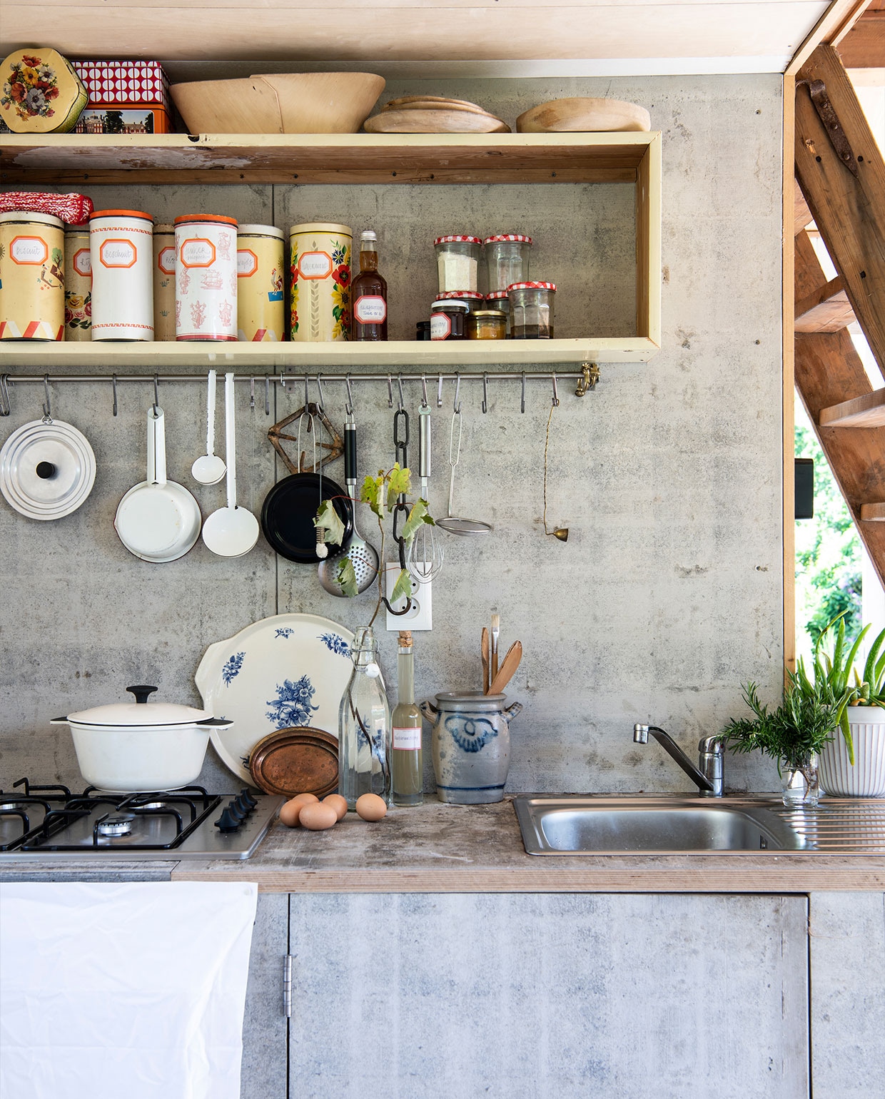 Keuken door Martin zelf gebouwd van steenschotten, waar ook het terras rondom het tuinhuis van gemaakt is. Witte braadpan Ikea, bord met blauwe bloemen erfstuk, Keulse pot vintage, railing met haken Ikea, houten borden HKliving, vintage beschuitbussen als voorraadblikken, lepels aan railing Van Manen aan Tafel, witte steelpan Dille &amp; Kamille. NEE | vtwonen TUIN special 5 | Productie Insidehomepage | Styling Myla Griese | Fotografie Louis Lemaire | Tekst Inge van Lieshout | Tekstbewerking Ina Babbé