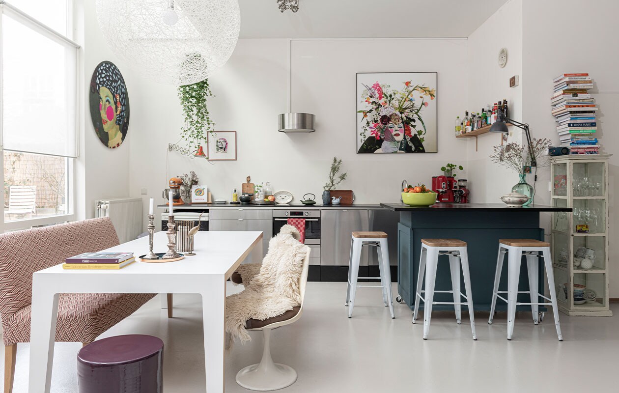 Roestvrijstalen keuken en afzuigkap Marktplaats, lades eronder zelfgemaakt. Bar zelfgemaakt van oude ladekasten van de kringloopwinkel. Op maat gemaakte tafel, barkrukken van Tolix, hanglamp Random Light van Moooi en bankje Marktplaats. De bank is bekleed met stof van Alaloes Object &amp; Interieur. Tulip Chairs Pastoe en Oranje wandlamp kringloopwinkel. Schapenvachten, theepot Bredemeijer, blauw vaasje West Germany en vogelschenkkan Noordermarkt Amsterdam. Keramieken kruk Serax Alaloes Object &amp; Interieur. Zwarte wandlamp Ikea. Vitrinekastje via Facebook-buurtgroep. Kunst aan de muur gemaakt door Noor. Vaas op bar, kandelaars en vogel op tafel Vossenplein Brussel. Oude schaal met deksel en snijplanken van oma. Overig onbekend. NEE | vtwonen binnenkijken special 12-2021 | Styling Sharon Roest | fotografie Caroline Martinot | tekst Eveline Stoel