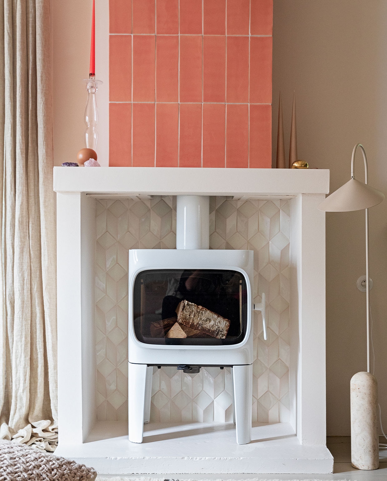 Houtkachel Jtul F305. Tegels 1030 cm kleur Flamingo Baby en witte tegels Constellation kleur Eggshell White via Quintalisque. Kussen Sukha. Lamp en kiezel Ferm Living. Glazen kandelaar herkomst onbekend. Kaarsen Ester &amp; Erik. vtwonen 02-2022 | styling Ilona Jongepier | fotografie Dana van Leeuwen