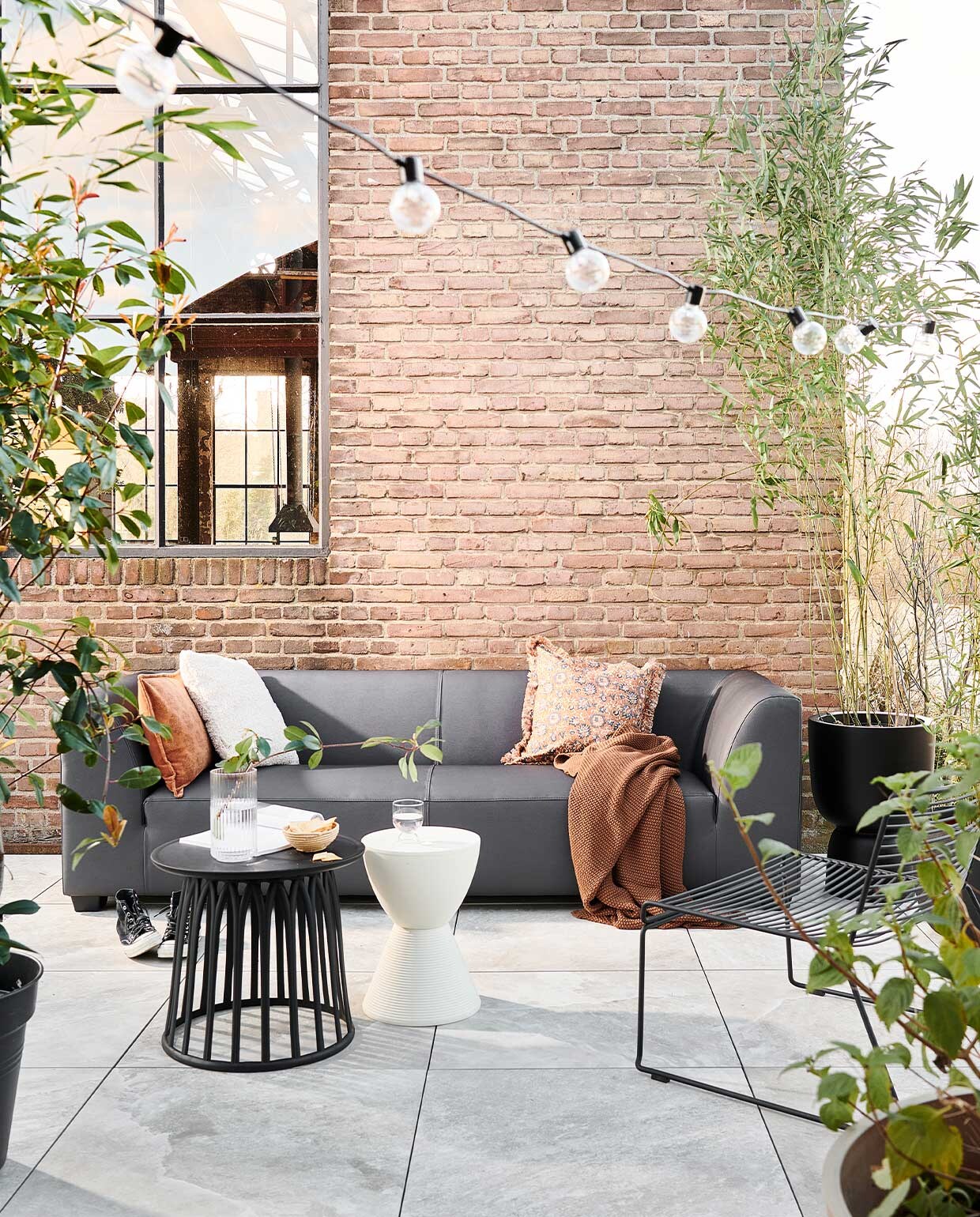 Buitentegels Solostone Uni Clouds 70x70x3,2 cm per m² € 69,95.3-zits buitenbank Hollandia van vtwonen € 1099,-, verkrijgbaar via basiclabel.nl, vtwonen.nl. M.m.v. vtwonen.be (kruk van Kartell, deken van Marc O’Polo, kussen van Bloomingville, lichtsnoer, hoge pot op voet van Elho, lage zwarte pot van Capi), basiclabel.nl (zwarte kunststof bijzettafel), com-anders (mand), vandijkenko.nl (stoel). vtwonen 04-2022 | Productie Tanja saarberg | Styling Marlies Does | Fotografie sjoerd eickmans