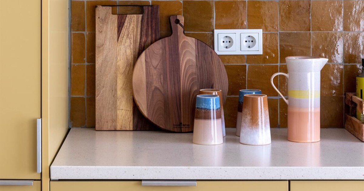 Flexa Creations muurverf om raam Midden Zandstrand (flexa.nl). Keukenkastfronten op maat gemaakt, prijs op aanvraag (k14.nl). Tegels achterwand Zelliges Mustard, per m² € 114,95 (householdhardware.nl). Houten planken van Bowls en Dishes vanaf € 15,-, koraalkleurige kandelaar van À la € 30,-, gele kandelaar Flare van Hay € 49,-, groene glazen vaas van Bloomingville € 38,90 (vtwonen.be). Vijzel € 28,44 (bowls-dishes.nl). Kan € 29,95 en theemokken € 11,40 van HKliving (eijerkamp.nl). Kunstwerk Neutrale collage van Laura Horn € 50,- (werkaandemuur.nl). vtwonen weer verliefd op je huis extra seizoen 15, aflevering 3 | styling Marianne Luning | fotografie Margriet Hoekstra