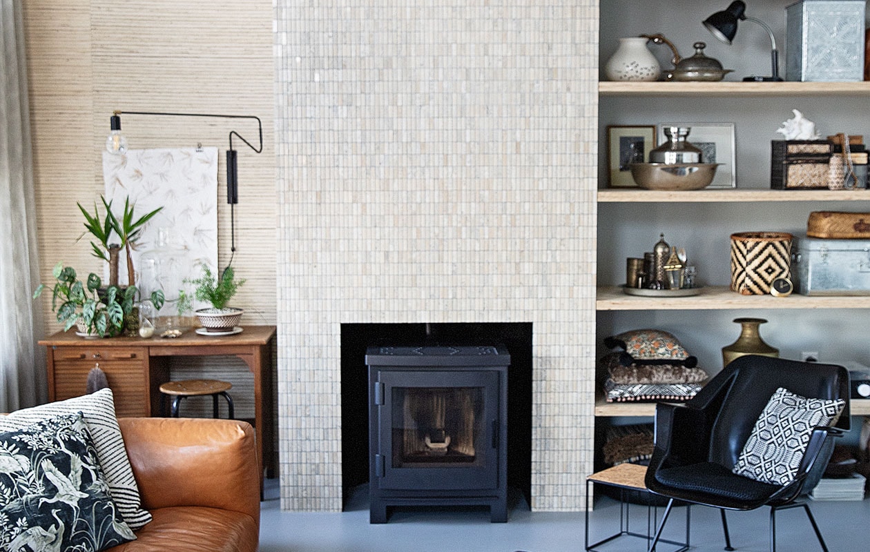 Behang Natural Wall Coverings Eijffinger, tegels natuursteen Praxis, muurverf Papyruswit Ral 8018 Flexa, plafondverf Powerdek Ral 9010 Flexa, planken underlayment. Kachel Arya van Nordic Fire, bureau kringloop Het Goed, zwarte wandlamp House Doctor, zandloper Laif &amp; Nuver, schelp Bij Risje Ameland. Witte lampen Praxis, snoer Snoerboer, bank Het Anker, dierenvel Ikea, vloerkleed Woontheater de Eclips, fauteuil Gispen 416 van Dutch Originals, bijzettafel en kussen vogel zelfgemaakt, kussen strepen Home Delight. Salontafel en waxinelichthouder HKliving, dienblad Ottomania. In kast: vaas met kraanvogels Piet Hein Eek, rotan mand Laif &amp; Nuver, bovenste kussen zelfgemaakt, middelste kussen Kleur op Kleur Interieur, onderste kussen Imbarro, platenspeler Crosley, grote schelp en Matroesjka Bij Lokaal, klok Karwei. Overig vintage of souvenir. productie en styling Ilona Jongepier | fotografie Dana van Leeuwen | tekst Anna van der Heijden