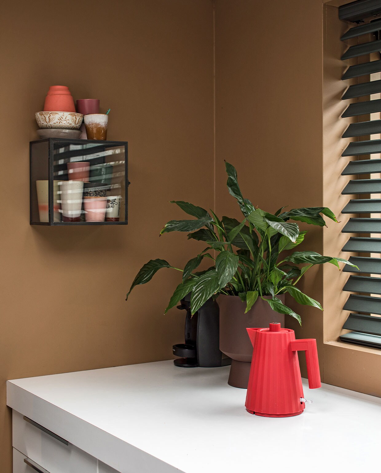 Muurverf Spiced Honey Flexa. Vitrinekast Ikea. Mokken HKliving, Hella Duijs, Nienke van de Pol. Servies kringloop. Koraalkleurig vaasje Hella Duys. Lepeltjes House of Oeli. Op aanrecht: bloempot Jysk, plant Ikea, rode theepot/waterkoker Alessi. Vlinderjaloezieën Bece raamdecoratie, Hubo. vtwonen 10-2021 | productie en fotografie Corine Hoge Bavel