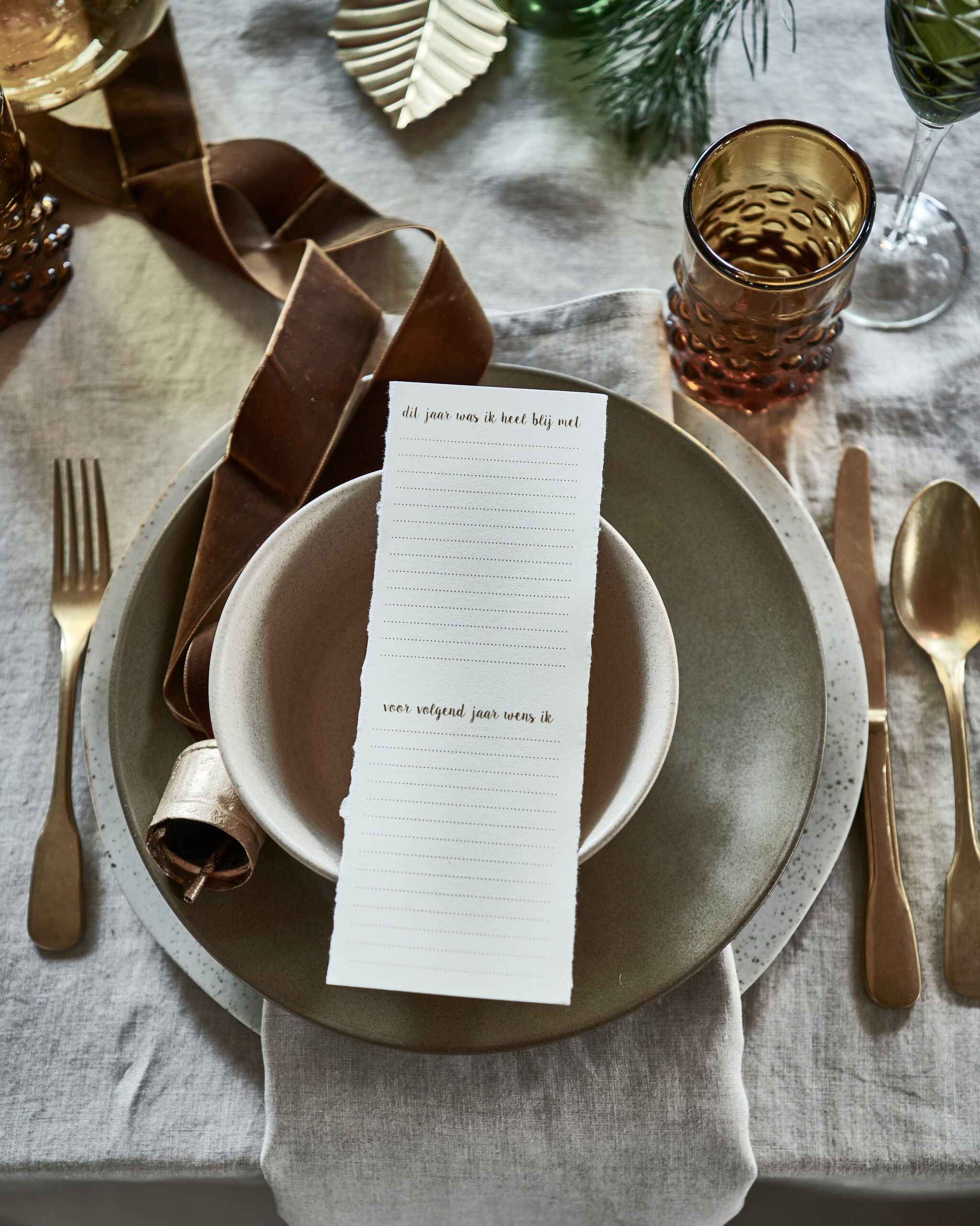 linnen tafelkleed € 39,99, servet, set van 2 € 9,99 (hm.com). Groen bord € 27,95, beige kom, groen ovaal bord, alles aardewerk van Studio Ro Smit (factor-ij.amsterdam). Beige bord € 25,- (nordal.eu). Groen champagneglas, set van 6 € 160,- (polspotten.nl). Gouden kerstbal in vorm van bel, set van 2 € 15,-, gouden blad, set van 3 € 6,- (bungalow.dk). vtwonen 12-2021 | styling Danielle Verheul | Fotografie Sjoerd Eickmans | Tuin van Judith (groenstylist), assistentie Niels Kist, Kula van den Broek