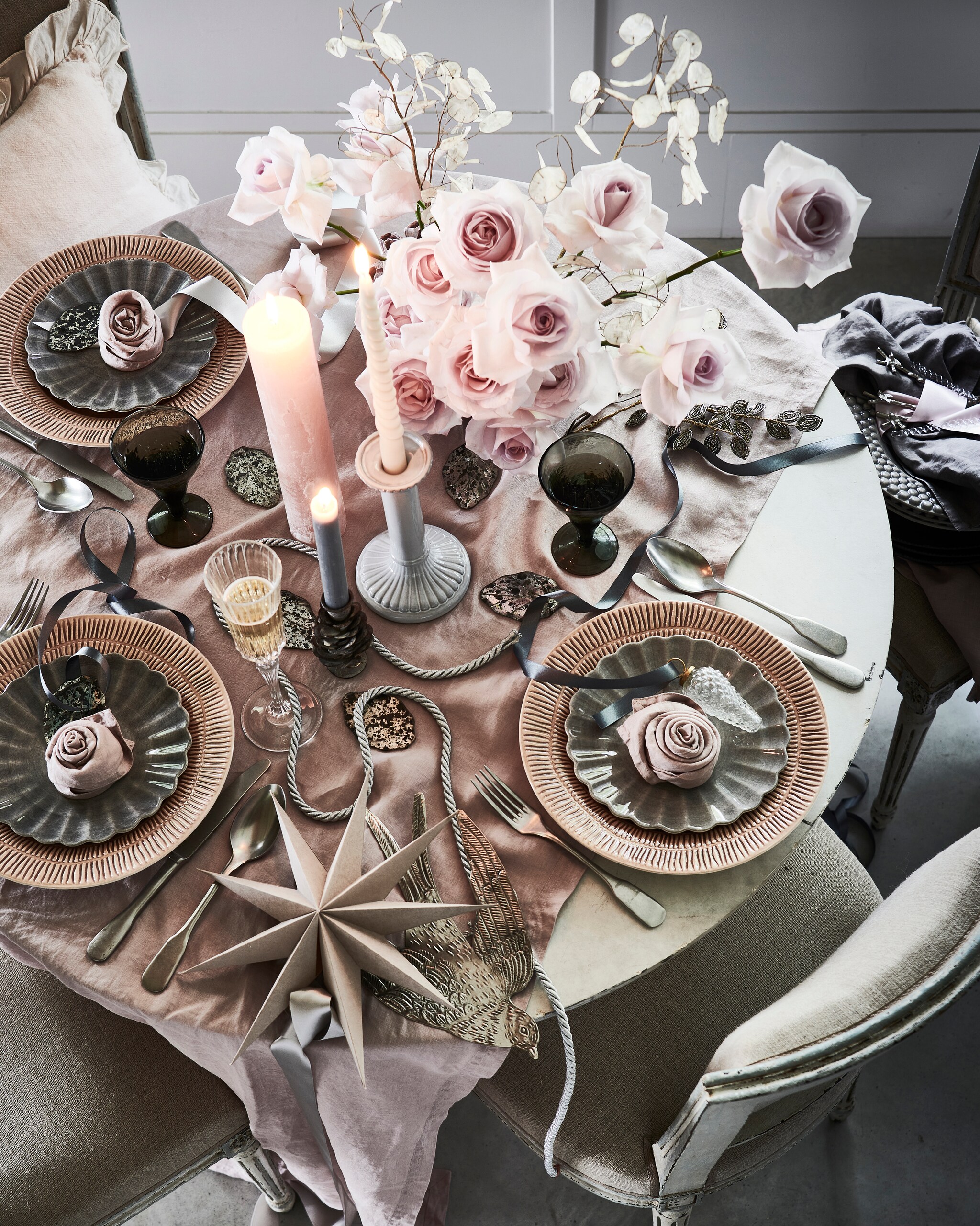 Bloemen, prijs op aanvraag (tuinvanjudith.wordpress.com). Tafel € 439,- (basiclabel.nl). Antieke stoelen, per stuk (pietjonker.nl). Linnen tafelkleed € 39,99, servetten, per set van 2 € 9,99, witte kandelaar € 17,99 (hm.com). Roze borden, per stuk € 29,50, grijze borden in bloemvorm, per stuk € 22,50, grijze borden met schulprand, per stuk € 30,95 (zwaanzinnig.shop). Roze kussen met volantrand € 22,99, champagneglas € 7,99 (zarahome.com). Zachtroze kaars € 14,- (allestedlund.com). Zinken kandelaar in vorm van dennenappel € 7,95, zilveren metalen zwaluw € 17,50, kerstdecoratie van kralen in vorm van blad, kerstbal dennenappel € 4,95 (weldaad.com). Grijze wijnglazen, per stuk (anna-nina.nl). Grijze papieren ster € 8,- (bungalow.dk). Theelepels van gedraaid glas, per stuk € 3,99, zilveren theelepels met vogel, per stuk € 4,99 (sissy-boy.nl). Interieurontwerp Piet-Jan van den Kommer (vandenkommer.nl). Overig privébezit. Tutorials over een roos maken van een servet staan op youtube onder servetvouwen.nl. vtwonen 12-2021 | styling Danielle Verheul | Fotografie Sjoerd Eickmans | Tuin van Judith (groenstylist), assistentie Niels Kist, Kula van den Broek