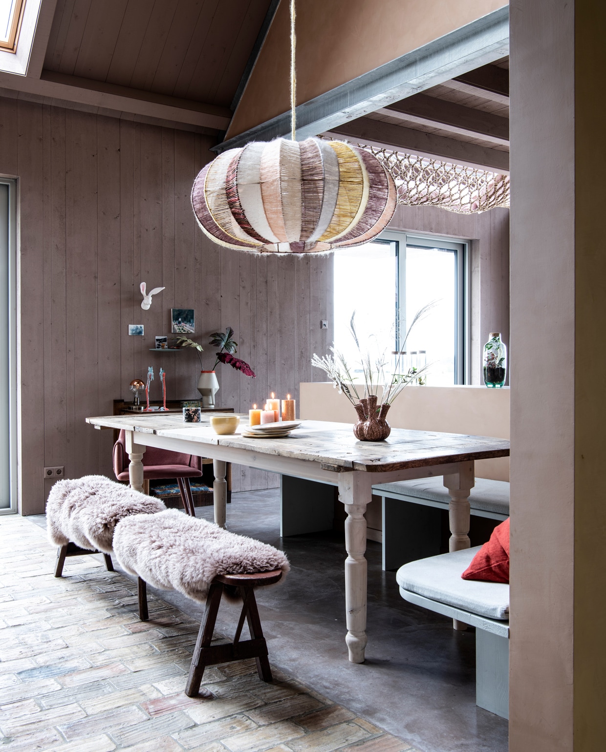 Hanglamp eigen ontwerp van Larissa, gemaakt door HeinsHome. Tafel zelfgemaakt van een oude deur, vergroot met tussenstuk. Onderstel Van Dijk &amp; Ko. Hoekbank maatwerk, in verfttint Soft Asparagus van Pure &amp; Original. Houten bank Marktplaats. Schapenvachten Ikea. Vaas op tafel lokale bloemenzaak. Schaal en borden keramist Loeke Pam. Kuipstoel Fonq. Rood kussen Wehkamp. Zitkussen hoekbank van recycle-denim via Annemieke Koster. vtwonen 11-2021 | styling Esther Jostmeijer | productie Insidehomepage | fotografie Louis Lemaire | tekst Inge van Lieshout | tekstbewerking Sunna Borghuis