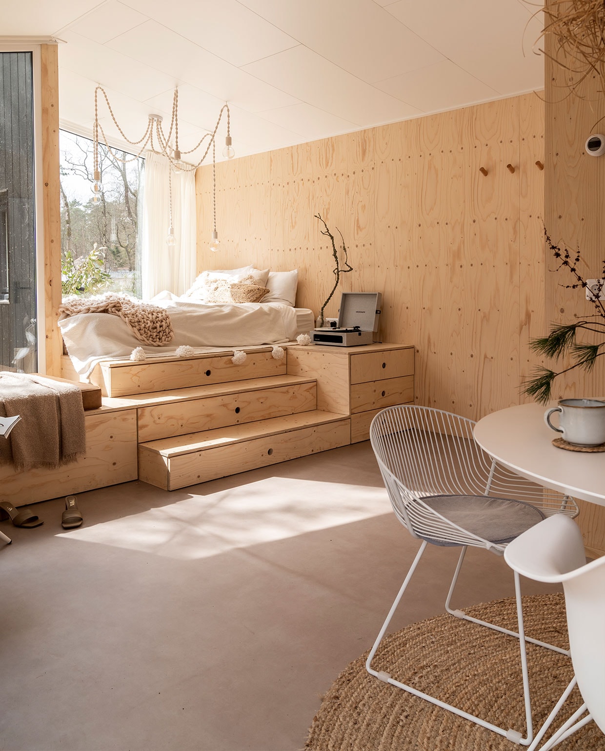 Bedombouw Hertog Recreatiebouw. Kandelaarlamp zelfgemaakt. Matras Emma, beddengoed herkomst onbekend, sprei met pompons gekocht in Marrakech, gehaakte sprei Lidl. Waterkaraf Ikea, tak uit het bos, platenspeler Crosley, beige kussen H&amp;M Home, bruin kussen Calma House. Tafel Wehkamp, draadstoel, stoelen Vintagelab15. Mokken Ikea, droogbloemen Bloomon en uit het bos, kleed Volero Vloerkleden. vtwonen 11-2021 | Fotografie Muk van Lil