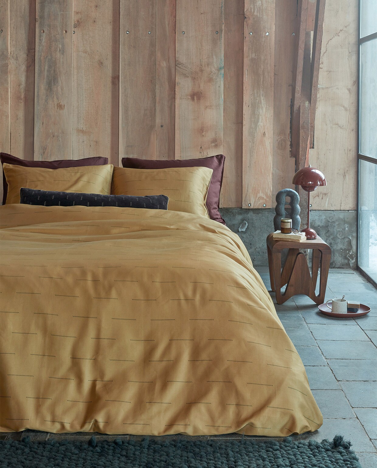 Dekbedovertrek Blurred Lines van katoensatijn, geel, 140×200/220 cm € 79,95, 200×200/220 cm € 149,95, 240×200/220 cm € 159,95. Kussen Velvet Crops Dark Red van fluweel, 30×90 cm € 49,95.M.m.v. kasstoor.nl (bijzettafel, tafellamp, vloerkleed), letoile.store (geurkaars, mok, theelepel, zeepjes), studio-yen.com (kunstobject). Overig privébezit. vtwonen 09-2021 | productie Tanja Saarberg | styling Danielle Verheul | fotografie Richard Smit