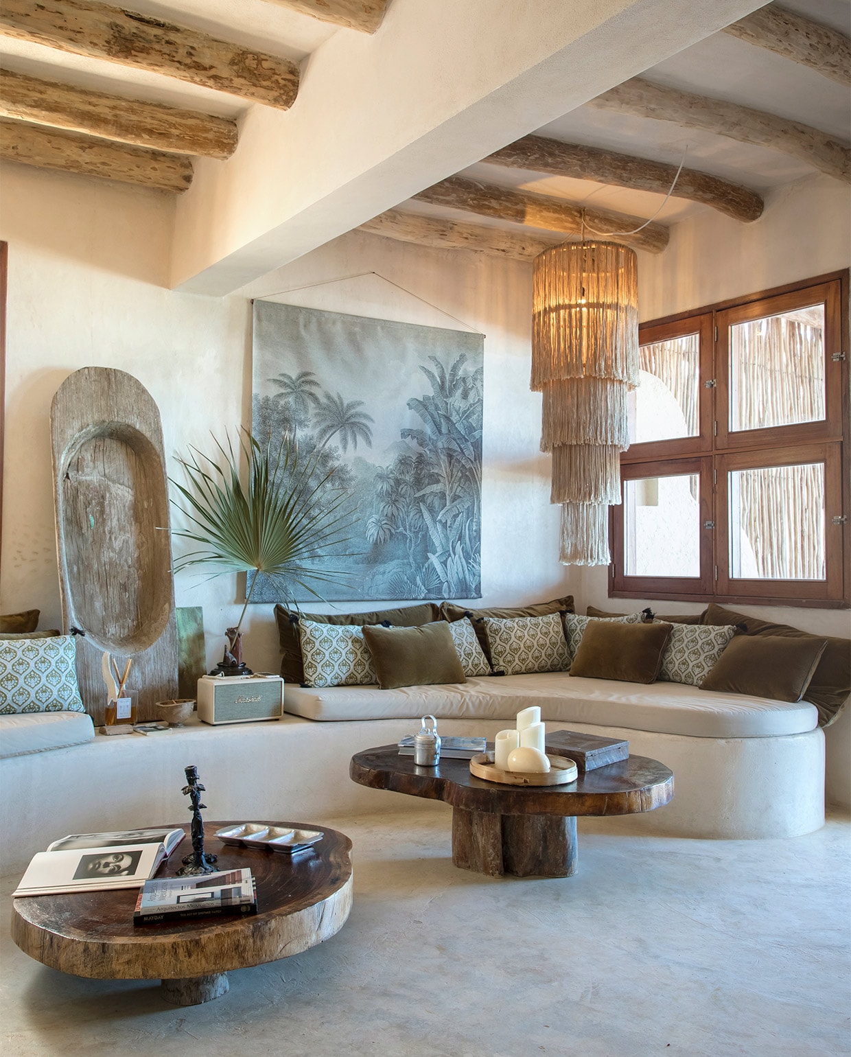 De golvende bank is gemaakt van cement met een coating van fijn zand. Kroonluchter en salontafels lokaal gekocht. Kussens Harmony Textile. Muurdecoratie Jungle van La Maison Pernois vtwonen special zomerhuizen 07-2021 | productie &amp; tekst Anne-Catherine Scoffoni\nfotografie Cécile Perrinet-Lhermitte\ntekstbewerking Eveline Stoel