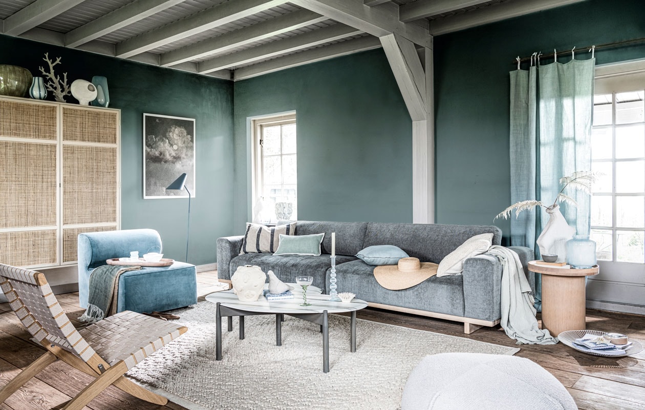 Krijtverf Polar Blue op de wand, per liter € 39,25 (pure-original.nl). Kast van HKliving, 125x40x200 cm (bxdxh) € 1495,- (vtwonen.be). Grijze keramieken vaas € 255,-, witte glazen vaas met blauwe streep € 41,-, blauwe glazen vaas met witte cirkel € 99,-, blauwe glazen karaf € 42,- (brostecopenhagen.com). Koraal op voet € 150,-, marmeren salontafels, 115x60x 37 cm (;xbxh) en 73x62x 33 cm (lxbxh), set van 2 € 2199,- (vantil.nl). Witte keramieken vaas op voet met gat € 35,99, keramieken object stekel € 29,99, lichtblauwe glazen vaas € 29,99 (sissy-boy.com). Gevlochten fauteuil € 726,-, plaid met blauw-beige kleurverloop € 139,-, ovaal houten dienblad € 105,-, vloerlamp € 780,-, stoffen vogel € 45,-, poef € 230,-, witmetalen schaal € 65,-, houten opberger met glazen deksel € 45,- (homestede.nl). Blauw waterglas € 9,95, notitieboekje met bloemprint € 19,95, cocktailglas op gedraaide poot € 15,95, blauwe glazen kandelaar € 21,95 (anna-nina.nl). Witte vazen, per stuk vanaf € 80,- (lanenahome.com). Witte porseleinen theepot € 74,-, grijze kom € 13,50 (serax.com). Blauw-wit kunstobject vaas van Dum Keramik € 492,- kunstobject vaas met schelpen van Josefina Feurst € 352,- (theodeto.com). Fluwelen fauteuil van Menu € 1350,-, vloerkleed van Menu € 800,- (designtales.nl). Karton geprint met een detail van schilderij Botafogo Beach van Eduardo de Martino € 35,- (repros.nl). 4-zitsbank Aya, 318x96x79 cm (bxdxh) € 1299,- (sofacompany.com). Schilderij op canvas € 850,- (mooswillemsen.com). Blauw gestreept kussen € 19,99, turkooizen kussen met witte rand € 22,99, blauw kussen met donkerblauwe bies € 19,99, hoed € 39,99, gebroken wit kussen € 19,99, plaid € 35,99 (zarahome.com). Houten bijzettafel € 439,- (bolia.com). Gordijn gemaakt van stof Brera Lino van Designers Guild, per meter € 72,- (wva.nl). Overig privébezit. vtwonen 08-2021 |  styling Danielle Verheul | fotografie Sjoerd Eickmans assistentie Niels Kist, Meike LintHorst | maatwerk Meta Poulain