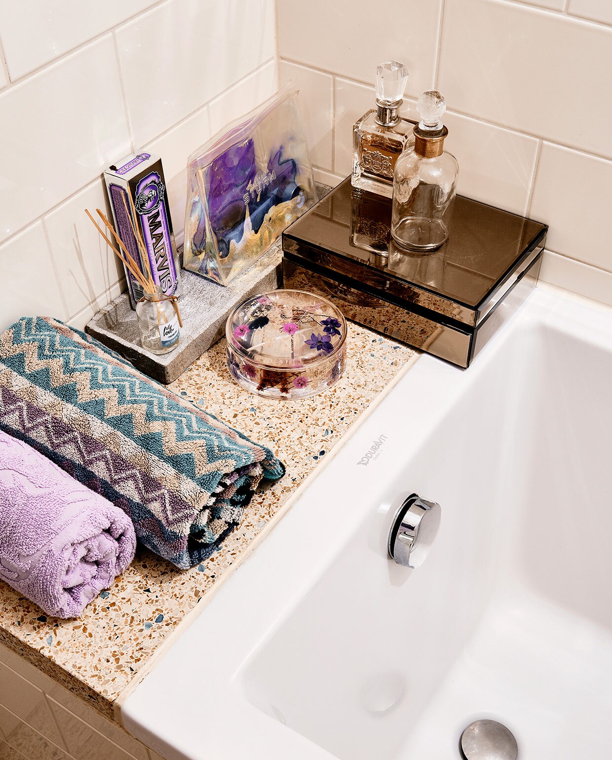 Lila handdoek en spiegeldoosje Zara Home. Handdoek dessin Missoni. Stenen tray onbekend. Doosje met bloemen Urban Outfitters. Parfumflessen Juicy Couture. Geurstokjes We Love the Planet. Tasje Barbara Sturm. vtwonen 06-2021 | productie CocoFeatures | fotografie Roos Oosterbroek