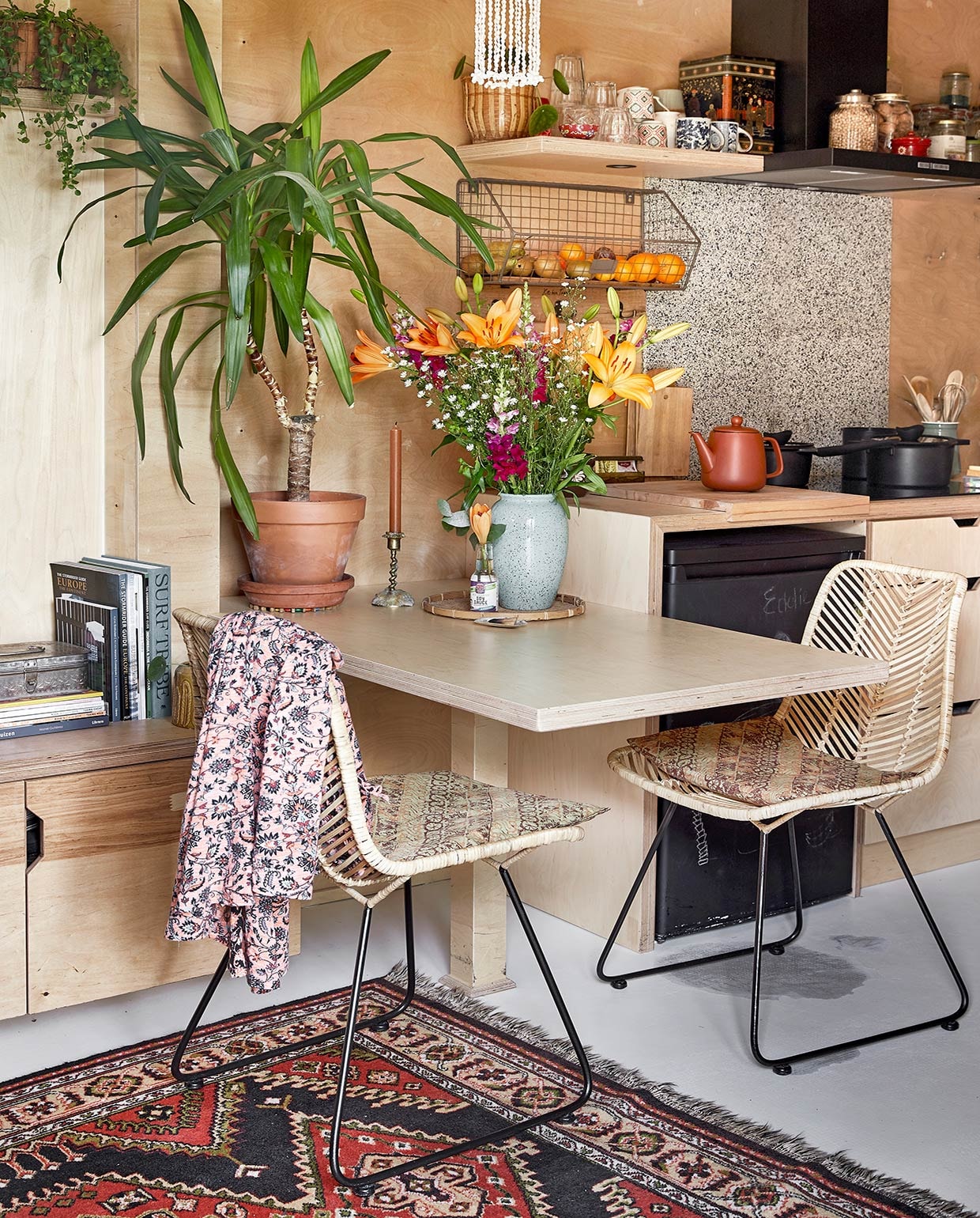 Vloerkleed van Carmens ouders geweest. Lage inbouwkast en eettafel zelfgemaakt. Stoelen Van Til Outlet. Onderzetter souvenir uit Indonesië. Flesjes en fruitmand Kitchen Trend. Glazen Duralex. Mokken Tastoe en kringloop. Voorraadpotten Clayre &amp; Eef. Hanglamp Curms. Theepot Xenos. Gietijzeren pannen en kookplaat herkomst onbekend. Achterwand kookplaat restpartij tegels gekregen van de buren. Keukengereihouder Dille &amp; Kamille. Vloer egaline gietvloer met Eurocol-coating. vtwonen binnenkijken special tiny houses 03-2021 | styling Iris van der Meer | fotografie Peggy Janssen