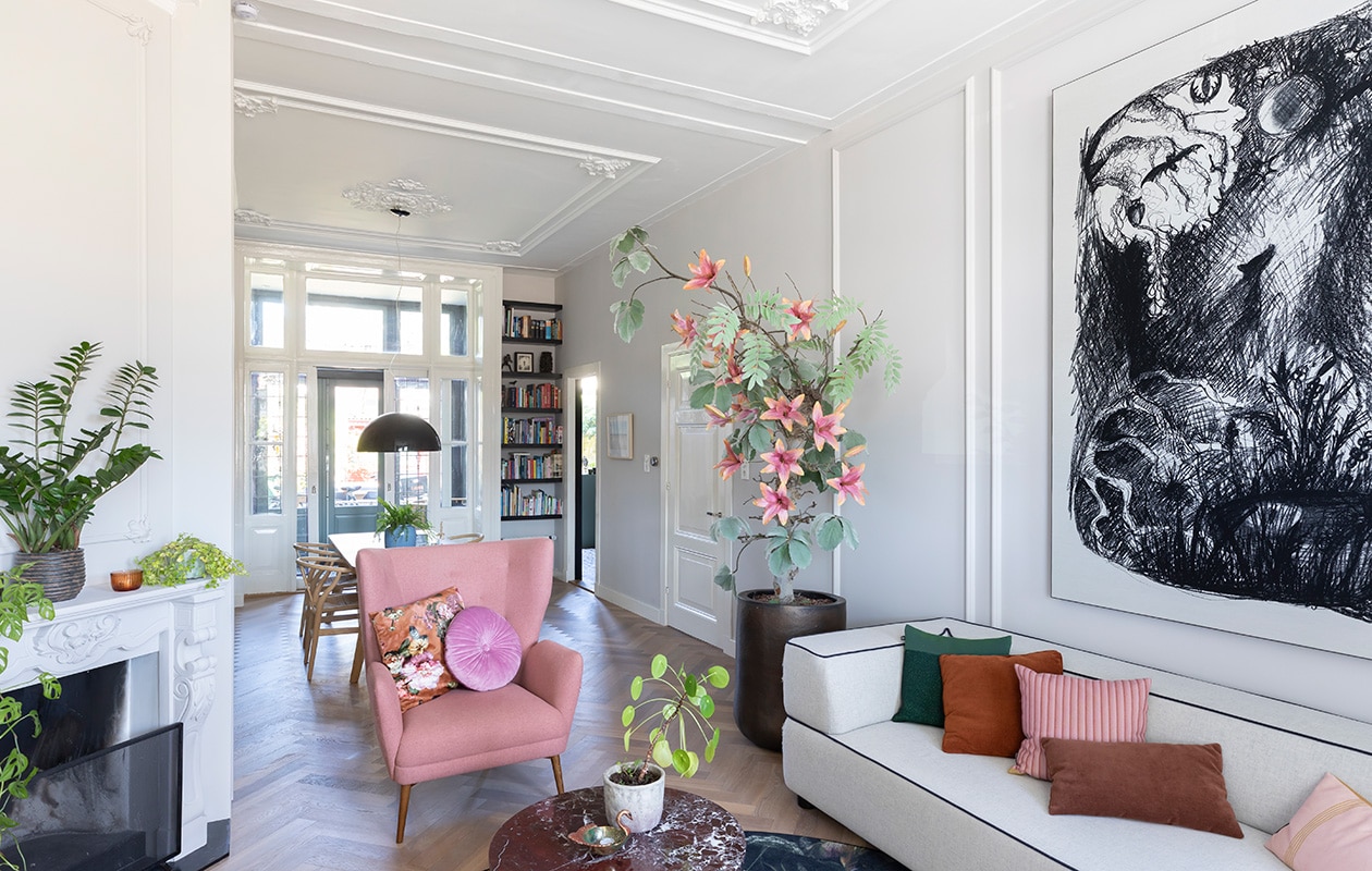 Muurverf Cornforth White Farrow &amp; Ball, massief eikenhouten visgraatvloer via Martijn de Wit Vloeren, boom ’s Zomers Bloemen, pot Domani, marmeren bijzettafel Westwing, pot Dekatuin, schaaltje op tafel Anna + Nina. Fauteuil Sofacompany, kussens op fauteuil Essenza, hanglamp Skygarden Marcel Wanders voor Flos, blauwe vaas HKliving, houten stoel Wishbone van Carl Hansen, wandplanken waren al aanwezig, geverfd in Pitch Black van Farrow &amp; Ball. Bank Fest Amsterdam, vloerkleed Moooi. vtwonen 01-2021 | productie en fotografie Margriet Hoekstra