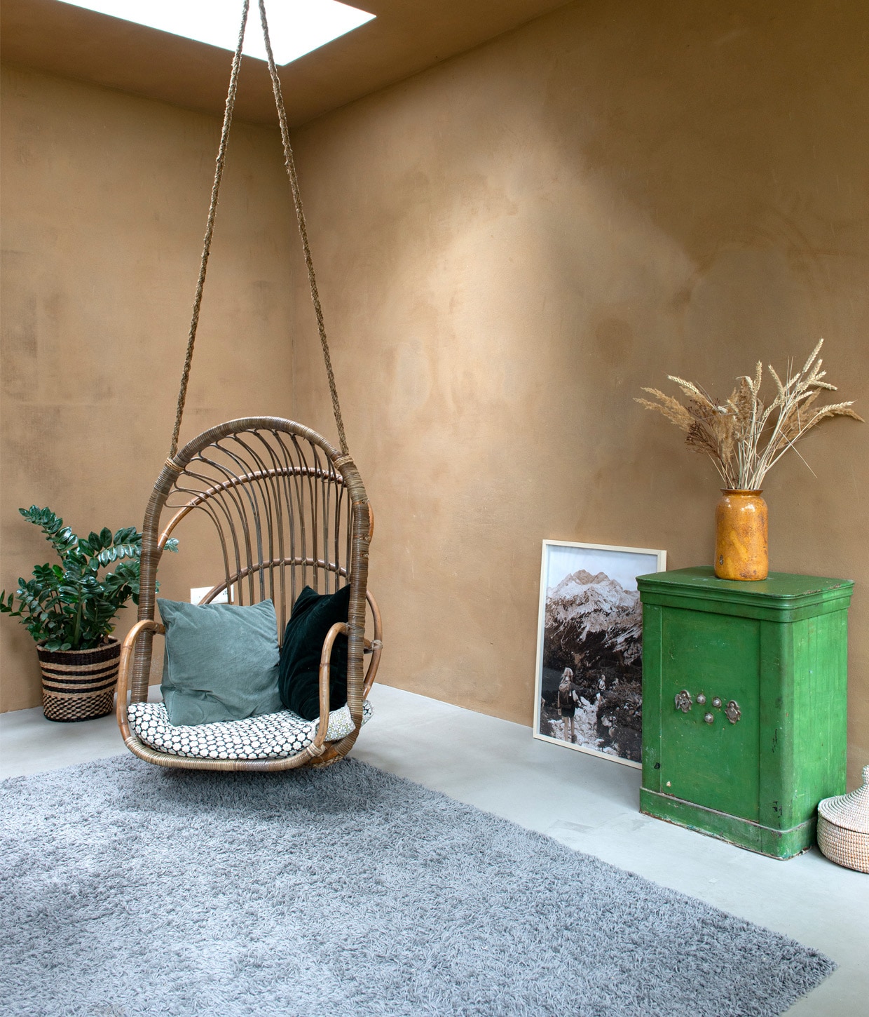 Rotan hangstoel van Marktplaats, kussens en mand om plant Ikea, deken in stoel gekocht in Kopenhagen, vaas vintage, kluis gekregen van een klant van Joost, eigen foto van een bergtocht vtwonen 01-2021 | Styling Esther Schuivens | Fotografie Caroline Coehorst