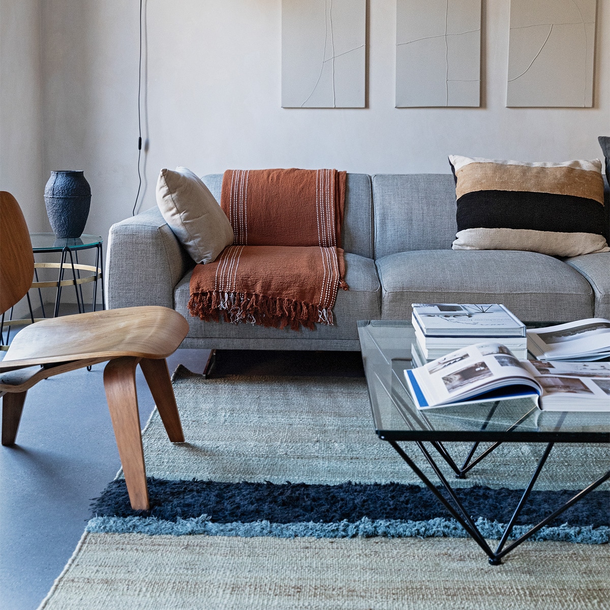 Kalkverf Mykonos van Bauwerk Colour, kunstwerken Vivienne Uzozie, wandlamp mini Lampe de Marseille van Nemo. Eames-stoel LCW Lounge Chair van Vitra. Bijzettafel Paul Lelieveld, vaas Serax. Bank Louter Design, beige kussen Zara Home, plaid H&amp;M Home, gestreept kussen The Corner Studio. Salontafel vintage Alanda Paolo Piva.