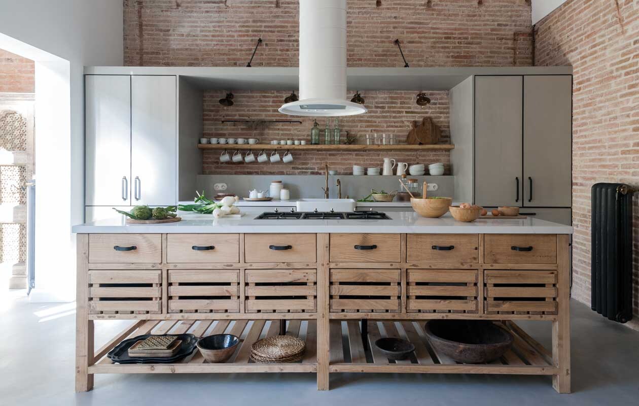 Frontjes van de keuken zijn van microcement, net als de vloer. Marmeren aanrecht van Compac, model Calacatta. Kraan Neve, gaskookplaat Smeg, de afzuigkap is eigen ontwerp en op maat gemaakt. Blikvangers zijn de ladekastjes, afkomstig uit het Indiase Rajasthan. Ambachtelijke houten schalen en wit porselein werden her en der verzameld. vtwonen 09-2020 | productie Vega Mg | fotografie Raül Candales | styling Susana Ocaña | tekst sunna borghuis\n