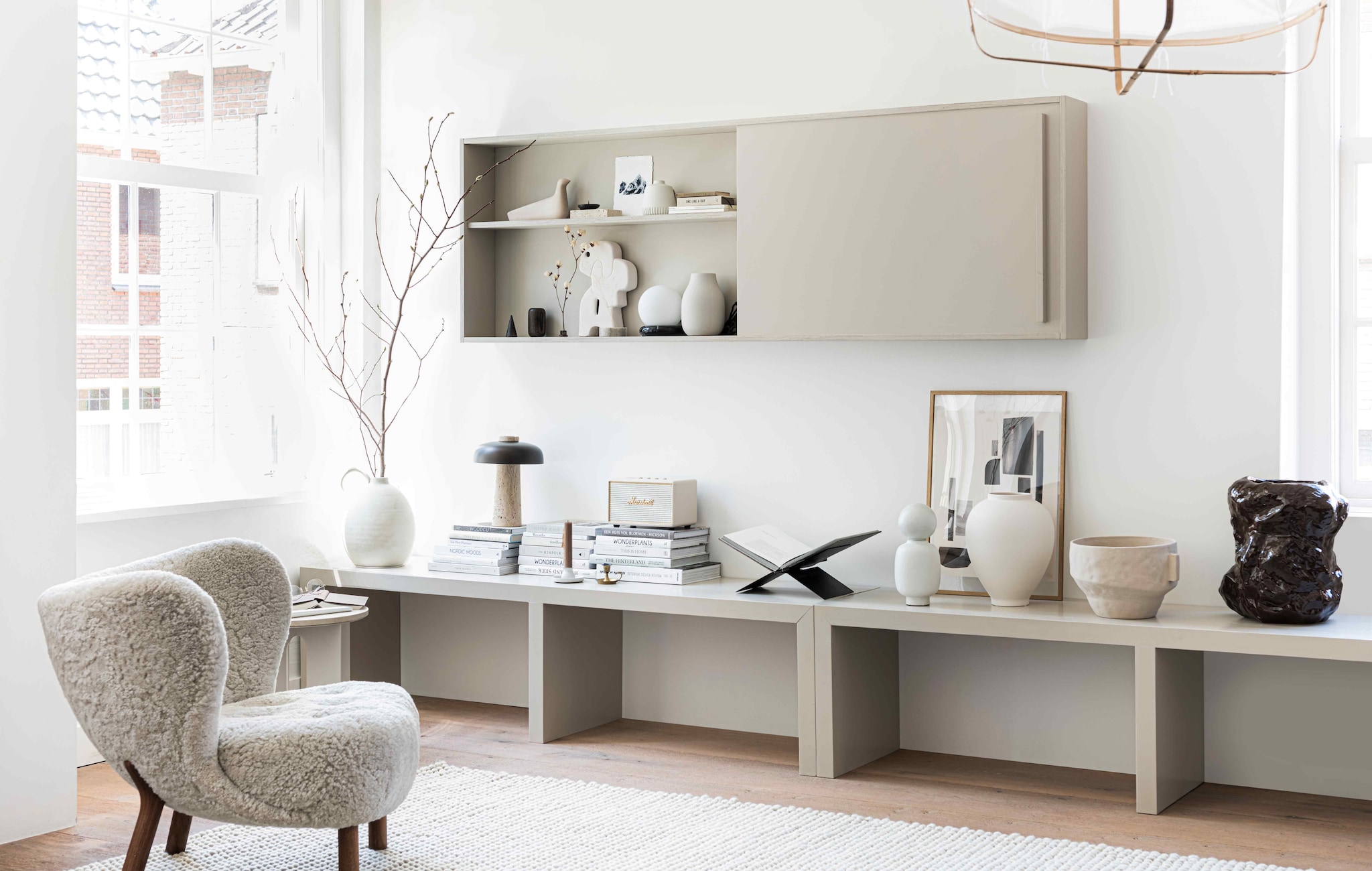 Fauteuil Little Petra van &amp;tradition € 2609,-, hanglamp van Ay illuminate € 429,- (flinders.nl). Vloerlamp JWDA met travertin voet € 1499,95, tafellamp met travertin voet en bronzen aluminium kap Reverse van Aleksandar Lazic € 550,- (menuspace.com). Vloerkleed Peas soft van Hay 300×200 cm € 935,-, witte vaas met boldop Muses Talia van Ferm Living € 79,- (vtwonen.be). Vaas met oor en grote witte vaas vanaf € 45,99, aardewerken kom € 45,99 (zarahome.com). Zwarte stalen boekenstandaard € 45,- (mendo.nl). Poster Shapes, 140×50 cm € 47,75 (facade-apt.com). Eikenhouten frame A3-formaat € 54,95 (moebe.dk). Crèmekleurige wifi-luidspreker Marshall Acton € 274,- (coolblue.nl). Mok € 14,50 (suhka.nl). Verfkleur sidetable en tv-meubel Rolling Fog (littlegreen.nl). Sidetable op maat gemaakt, prijs op aanvraag (richardvanmeerveld.nl). In de kast: houten vogel L’Oiseau van Vitra € 108,-, wit ornament Chulucanas van HKliving € 39,-, beige vaas Colora van Blomus € 36,95, tafellamp zwarte ring met witte bollamp van Ferm Living € 199,- (vtwonen.be). Overig privébezit. styling Kim van Rossenberg | fotografie Sjoerd Eickmans