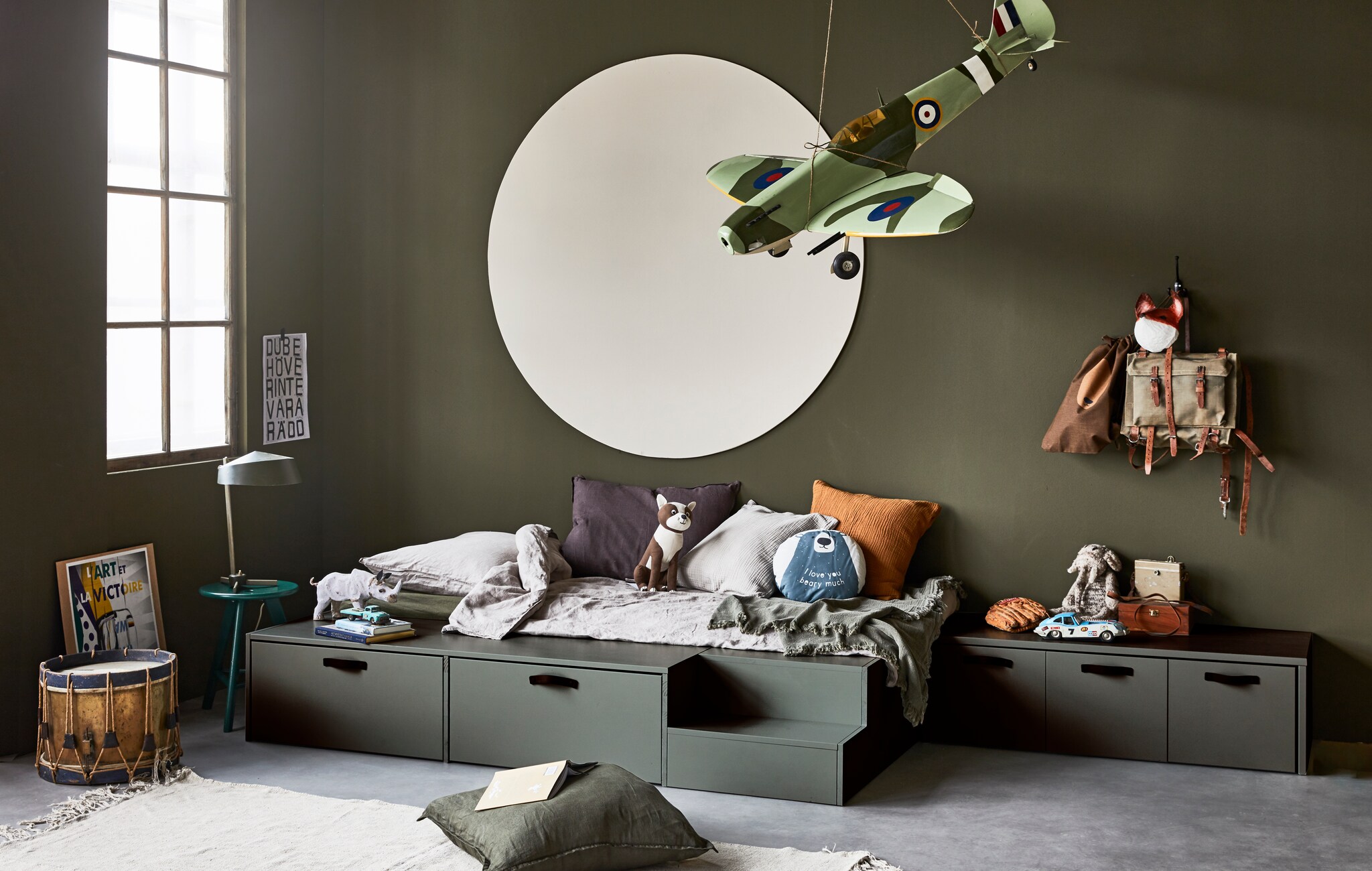 Ladenbed Stage van geschuurd grenen in kleur Soap, 35x204x131 cm (hxbxd), inclusief kast met 2 laden en trapje, exclusief matras (80×200 cm). Kistbank Stage van geschuurd grenen in kleur Soap, 36x120x50 cm (hxbxd).M.m.v. hm.com (linnen dekbedovertrekset, rond kussen beer, hond, zand en okergeel kussen, bruin tasje), wildschut-antiques.com (antiek vliegtuig, trommel), neeflouis.nl (bureaulamp, kruk) vtwonen.nl (vloerkleed van HKliving, donkerbruin kussen van vtwonen), zarahome.nl (groen sprei, linnen kussen), karwei.nl (muurverf camouflage, muurverf flax in stip). Overig privébezit. vtwonen 4-2020 | productie Tanja Saarberg | styling Cleo Scheulderman | fotografie Jeroen van der Spek | studio en decorbouw Milo Kol