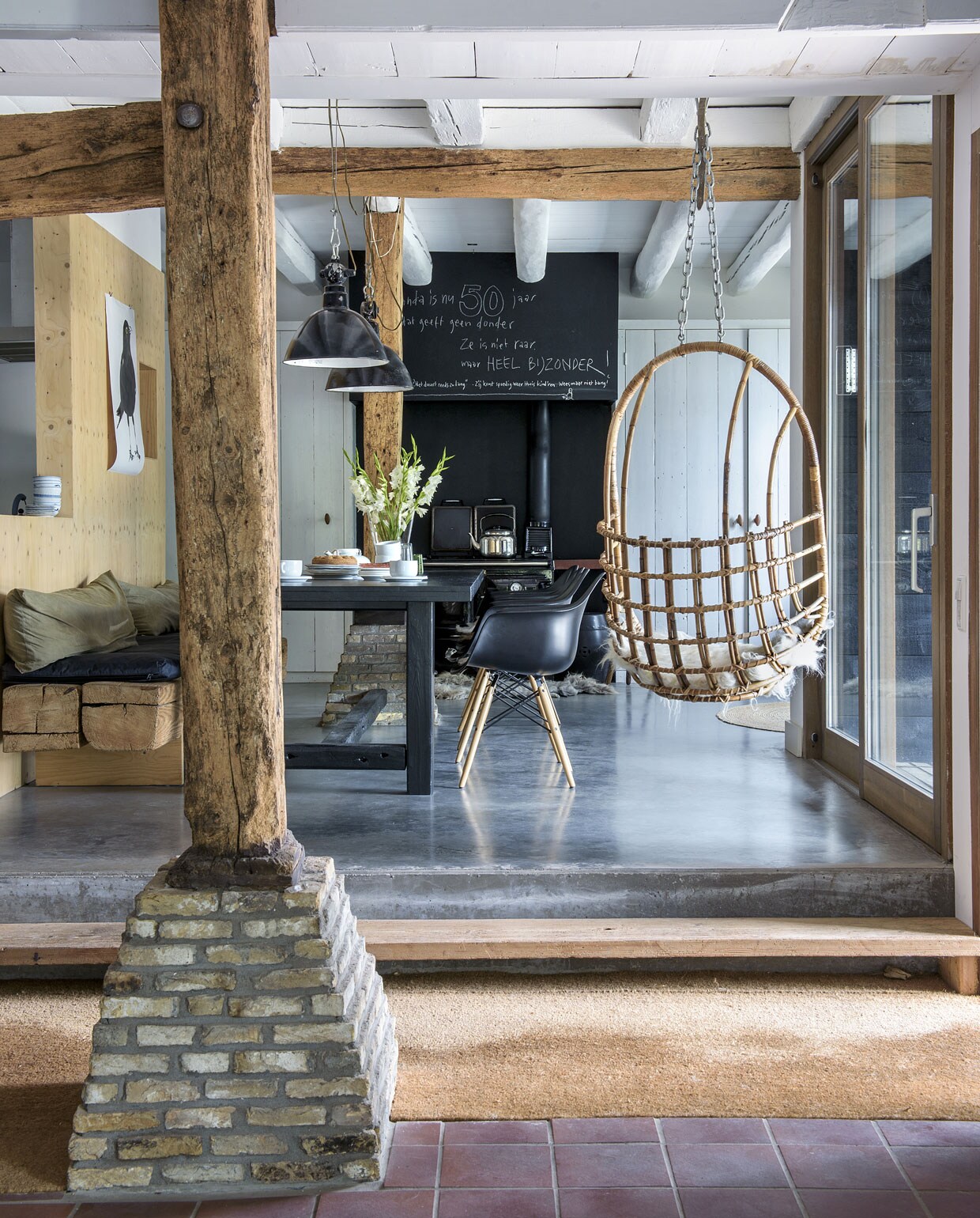 De tafel en het bankje werden zelfgemaakt van materialen uit het huis. De zwarte stoelen zijn van Eames. Lampen van Buitengewoon Brocante. De kruk was van Dietriks vader. Illustratie Maartje van den Noort. De oude staander loopt door tot aan het dak. De vloer is van beton. vtwonen 11-2019 | styling Monique van der Pauw | fotografie Ton Bouwer