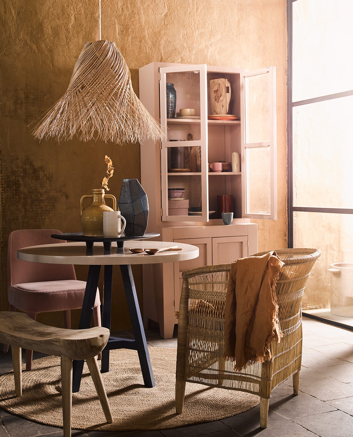 Ronde tafel met blauwe poot, roze kast (com-anders.nl). Hanglamp, gele vaas met oren, rond vloerkleed maat L, zwart dienblad, roze doos in kast, houten bord in kast, oranje bord in kast, bruin bord in kast, geel schaaltje, blauwe vaas linksboven in kast (loods5.nl). Bruin tafelkleed, snijplank, paarse kan, slabestek, bruin potje met deksel in kast, roze mok in kast (hm.com). Blauwe mok, blauwe vaas op tafel (thingsilikethingsilove.com). Roze schaal op poot van HK Living (wonenmetlef.nl). Houten vaas in kast, paars schaaltje in kast links onder, lila schaaltje onder in kast (householdhardware.nl). Pot buiten, rode vaas in kast, beige vaas in kast middelste plank rechts (serax.com). Witte kan op tafel (annemiekebootsceramics.nl). Houten bankje van Mica links (vtwonen.nl). Roze stoel van stof (edha-interieur.nl). Stoel gevlochten hout (archive-store.nl). vtwonen 06-2019 | styling Liza Wassenaar | fotografie Alexander van Berge