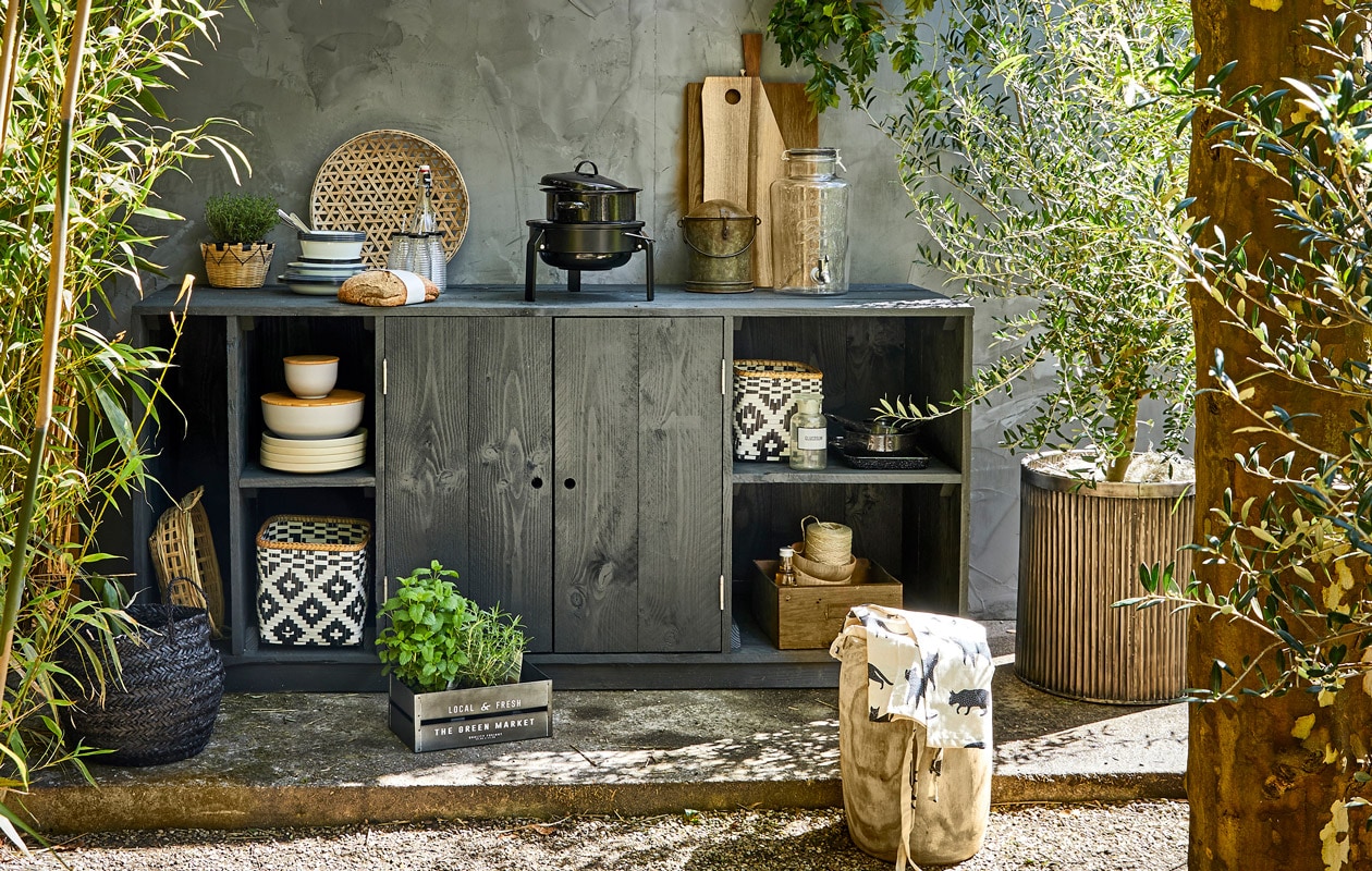 Geribbelde metalen plantenpot, ronde bus met deksel uit India (De Weldaad). Houten kruk, bamboe schalen met houten deksel, grote zwarte emaillen pan, kleine zwarte pannen, ecru borden, zwarte mand, naturel mand in kast set van 4, mandje met plant (Madam Stoltz). Glazen limonadetap, zwart-witte manden, witte emaillen borden, diepe borden, emaillen kommen, flesjes met zwarte dop en rietje (Nordal). Tafelkleed als schaduwdoek, schort, metalen kratje (H&amp;M Home). Laatje van metaal en hout (Burbri Antiek). Gevlochten schaal, houten kommen (HK Living). Barbecue Korpön (Ikea). Overig privébezit. styling Cleo Scheulderman | fotografie Jeroen van der Spek