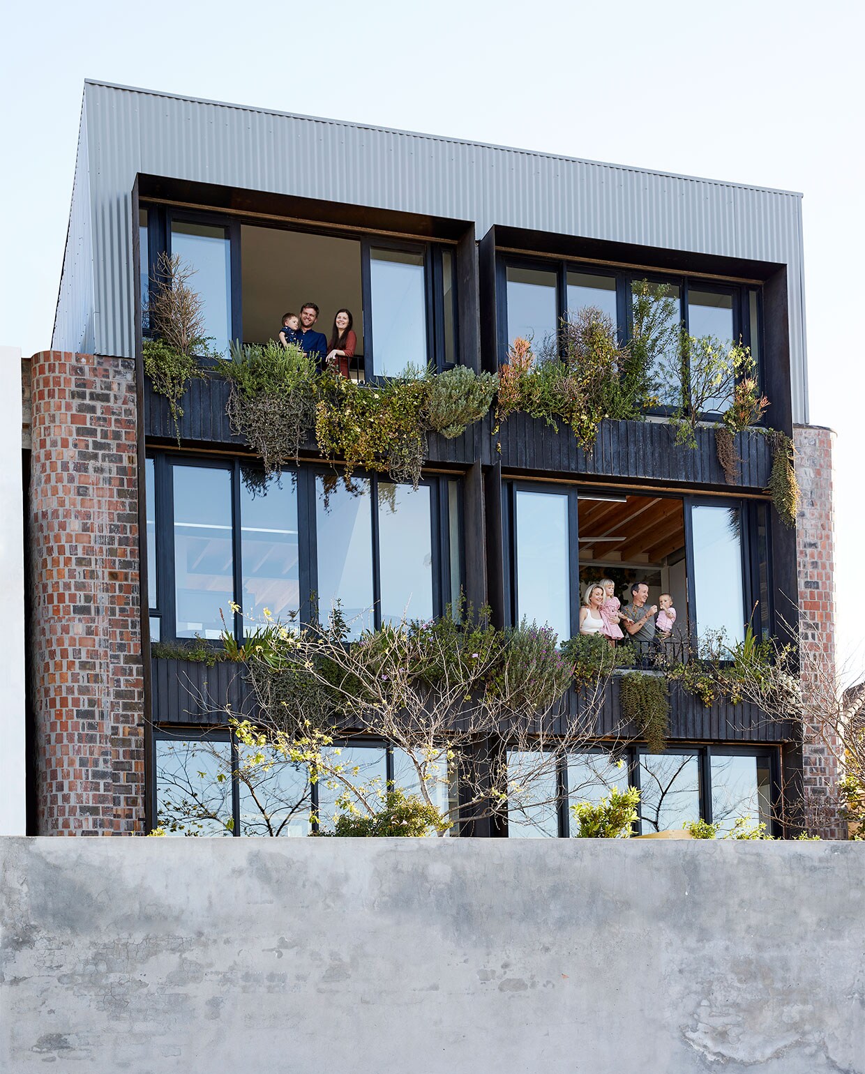 Stephen en Tanja met zoon Daniël (linksboven) wonen in het zwarte huis, David en Bonnie met kinderen Frankie en Grayson in het witte huis. De grote schuiframen hebben balustrades, waardoor de kamers heel open voelen – als balkons. vtwonen special binnenkijken 03-2022 | productie Bureaux | fotografie Warren Heath | styling Sven Alberding