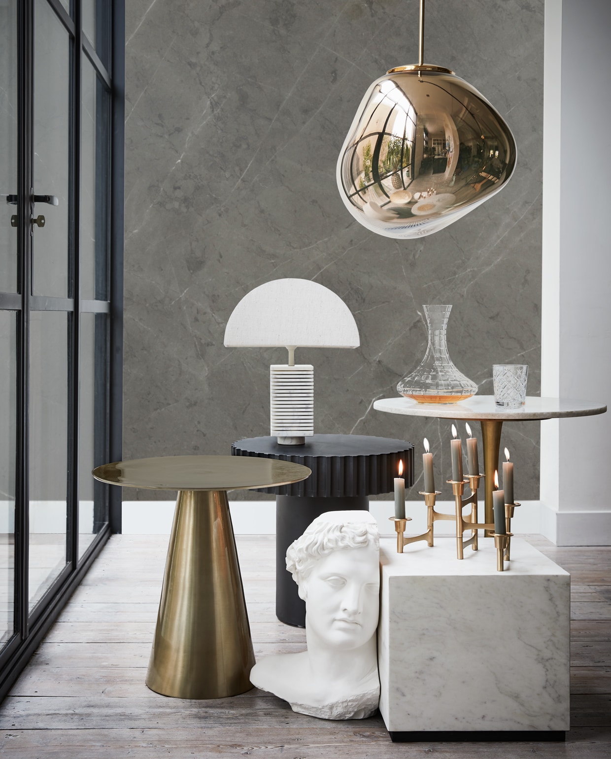 Messing tafel 45×49 cm (hxØ), zwarte tafel, witte marmeren tafel, gipsen beeld Apollo, tafellamp (hkliving). Hanglamp Tom Dixon van Loods 5 Design (loods5). Kandelaar (vtwonen.be). Karaf (polspotten). Glas Frasera (ikea). De achterwand is behangen met een custom made behangpaneel met daarop een uitvergrote afbeelding van wandtegel Classic Antracite Mat van vtwonen (vtwonen.be/vtwonen-collectie). vtwonen 13-2019 | styling Fietje Bruijn | fotografie Alexander van Berge