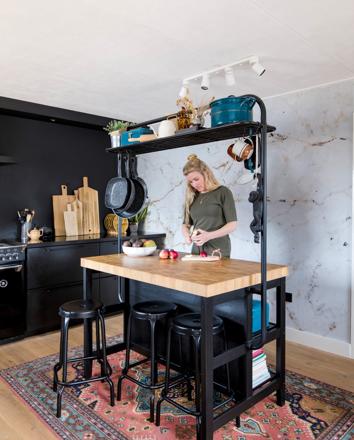 Keuken, hoge tafel, krukken en plafondlamp Ikea. Fornuis en afzuigkap Stoves. Karpet, blauwe emaillen pan, beschuit- en broodtrommel familiestukken. Marmerbehang Graham &amp; Brown. Bruine theepot, hangende seventies mokken, apothekerspotten en okergele borden kringloopwinkel. Zwarte theepot Bredemeijer. Snijplanken van Broodt, Xenos, Hema en Ikea. Fruitschaal Bowls and Dishes, hangende pannen Blokker. Muurverf Off Black Farrow &amp; Ball.