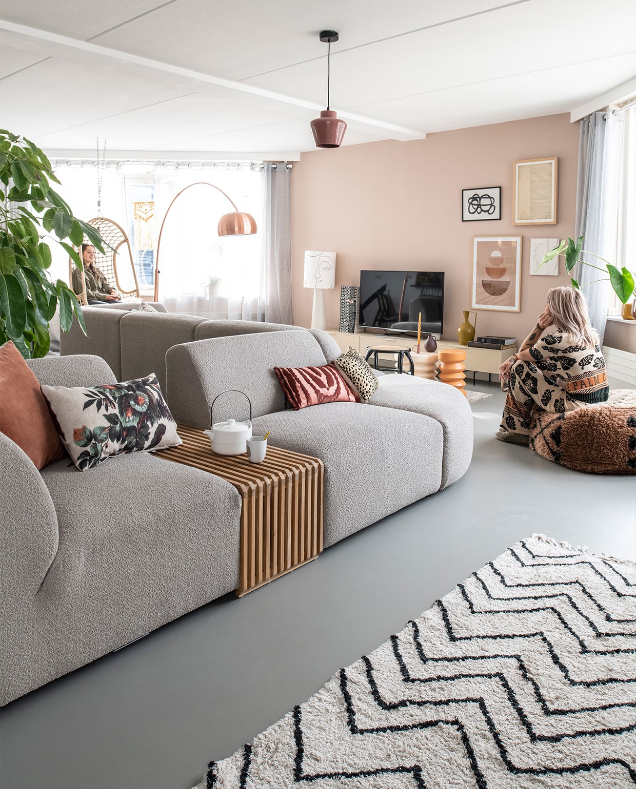 Muurkleur Zeester van Flexa, gietvloer Evolve. Bank en elementen Jax van HKliving. Theepot Home Society, beker Dassie. Kussens, hangstoel, staande lamp, dressoir, bijzettafels, rotan krantenbak en zigzagvloerkleed HKliving. Kunst op de wand: linksboven Sissy-Boy, rechtsboven HKliving, linksonder Incado, rechtsonder HKliving. Vloerkleed achter de bank en poef Aai Made With Love, booglamp Zuiver, hanglamp Woood. Kandelaar Branded, kaars Ravie, okergele plantenpot BePureHome.