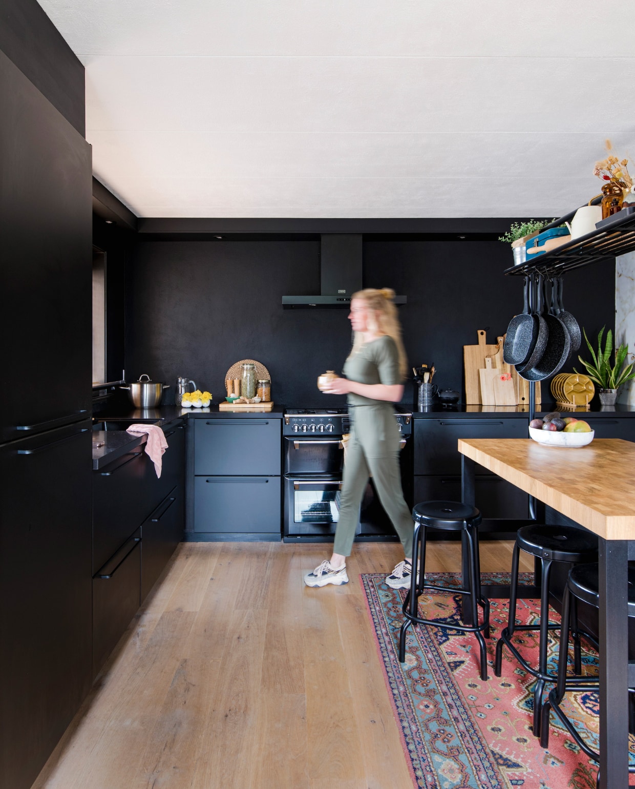 Keuken, hoge tafel en krukken Ikea. Fornuis en afzuigkap Stoves. Karpet en blauwe emaillen beschuittrommel familiestukken. Okergele borden kringloopwinkel. Zwarte theepot Bredemeijer. Snijplanken van Broodt, Xenos, Hema en Ikea. Fruitschaal Bowls and Dishes, hangende pannen Blokker.