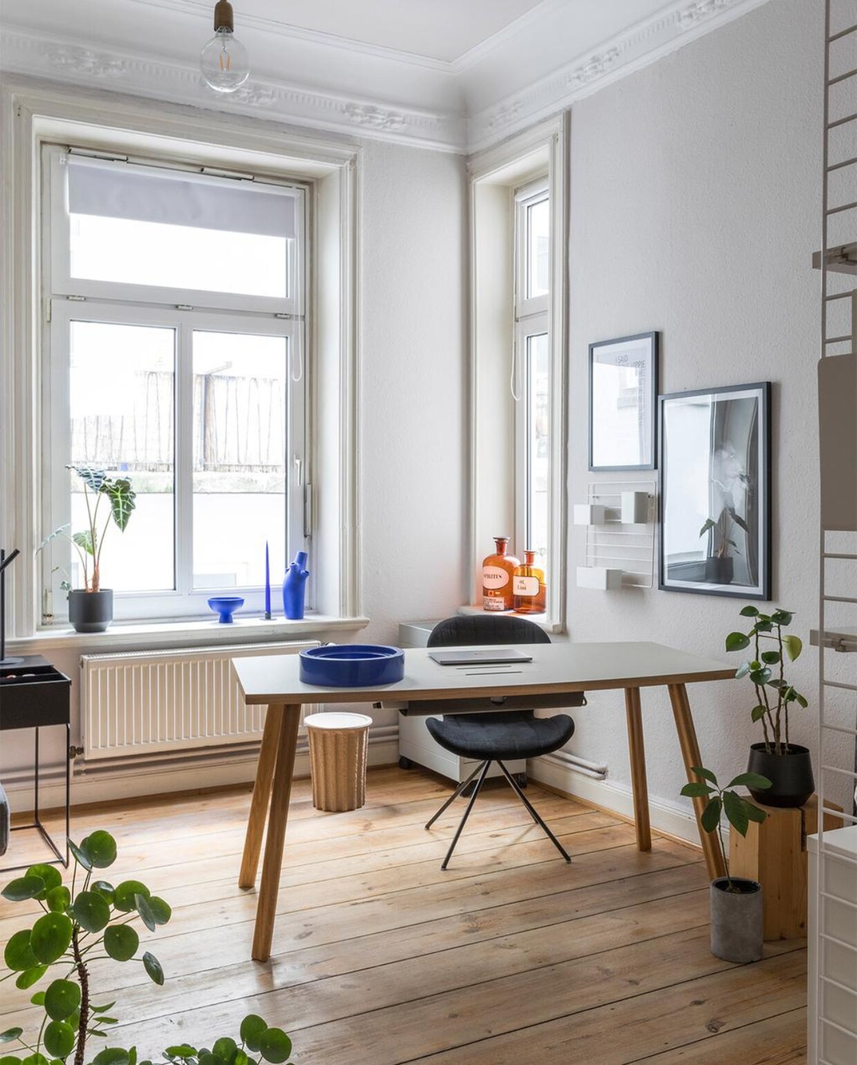 Muurverf Kolorat. Bureau Faust Linoleum. Stoel Zuiver. Plafondlamp House Doctor. Zwartwitfoto zelfgemaakt. Blauwe schaal in vensterbank raawii. Blauwe vaas vintage. Wandkast String Furniture. Bloempotten H&amp;M Home. Overig onbekend.