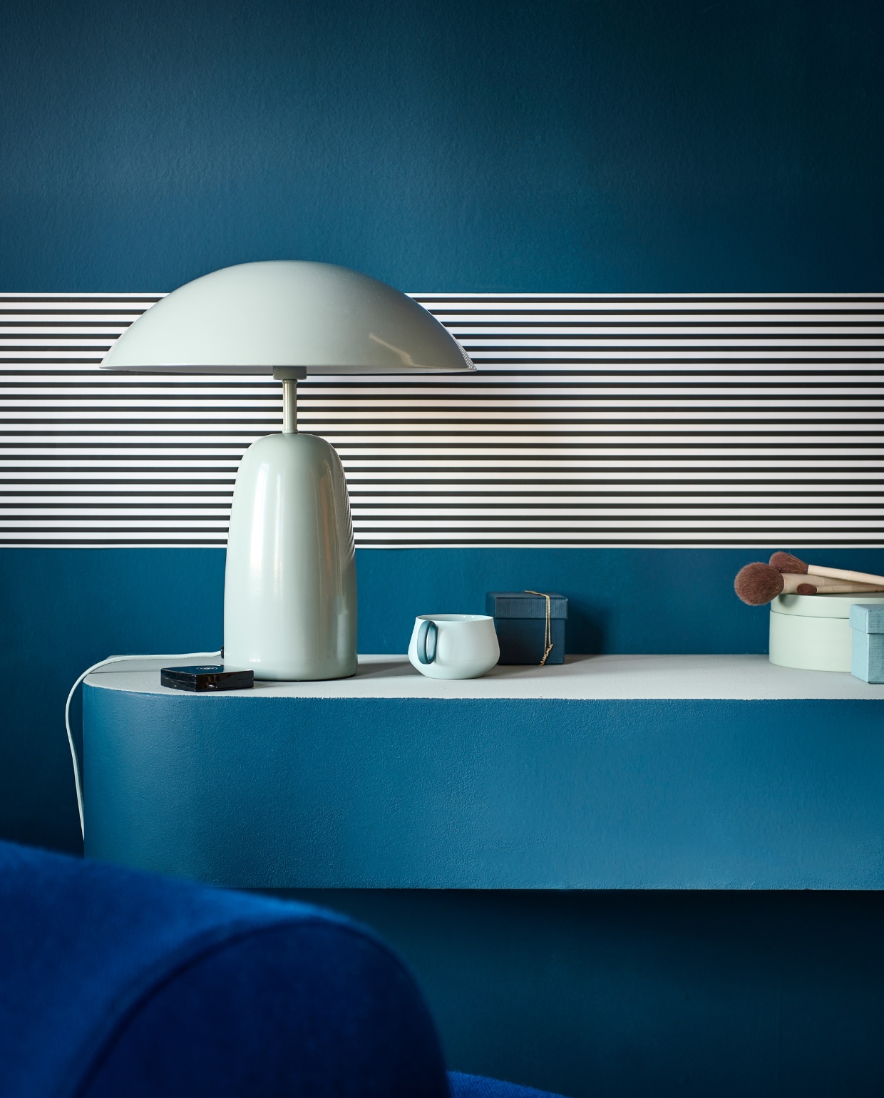 Muurverf buitenkant en onderstel make-uptafel en wand Denim, bovenkant make-uptafel Soap van vtwonen, 1 liter € 23,99, 2,5 liter € 39,99. Behangstrook Streep Pitch Black/Egg White van vtwonen, rol 10 m x 100 cm € 14,99.M.m.v. hm.com (tafellamp, sieradendoos), festamsterdam.nl (fauteuil), dumu (theekop). Overig privébezit.