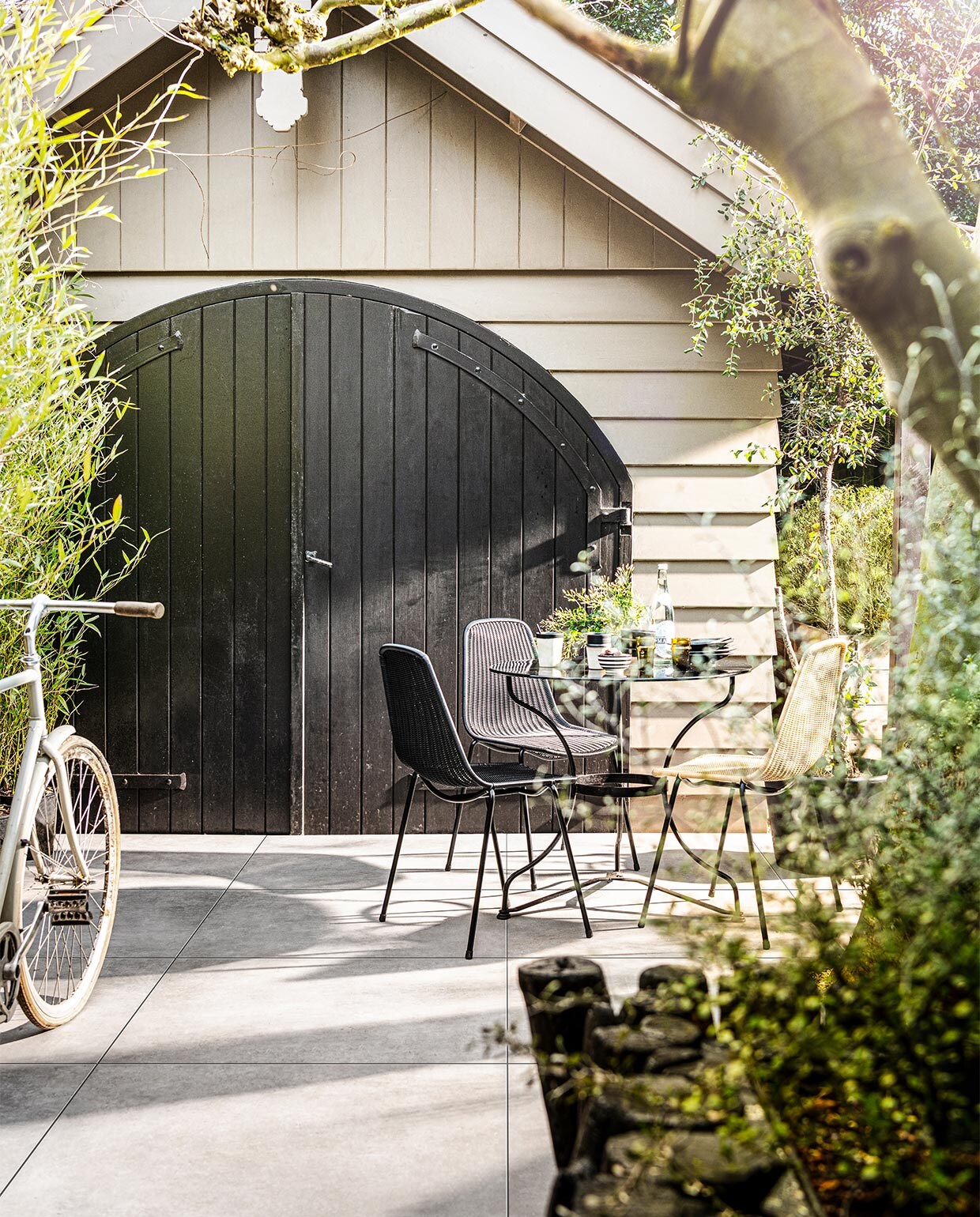Tegels Solostone Uni Mold Grit, 90x90x3 cm (lxbxh) per m² € 80,- (ook verkrijgbaar in Basalt, en in Grit, Basalt en Taupe in 70x70x3,2 cm). M.m.v. householdhardware.nl (servies, mokken, glazen, schaaltje), bymolle.com (stoelen Basket Chair). Overig privébezit.