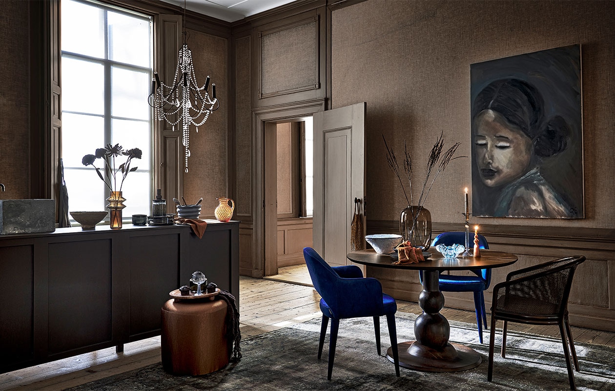 Keuken gemaakt door Combitex, prijs op aanvraag (com-anders.nl). Linnen schort € 29,99, keramieken lepels, per stuk € 9,99, dienblad op pootjes € 34,99 (sissy-boy.com). Bruin linnen servet € 4,50, bruine glazen karaf € 100,- (paviljoennoord.com). Papier-maché schaal € 39,95, bruine glazen vaas € 49,95, voorraadpotten met houten deksel, per stuk vanaf € 21,95, wijnglas op blauwe poot € 10,40, blauwe schaal met streeptextuur € 33,60, lichtblauwe schalen, per stuk € 34,90, donkerblauwe borden, per stuk € 16,95, donkerblauwe kommen, per stuk € 19,95, blauwe glazen schaal € 39,-, blauwe glazen kandelaar € 29,95, eetkamerstoel met webbing rugleuning € 649,- (nordal.eu). Metalen bloemen, per stuk € 19,95 (hamptonsbergen). Kroonluchter € 1450,- (brechtjeolsthoorn). Bruine gestoffeerde poef vanaf € 332,75 (rapture.amsterdam). Vloerkleed prijs op aanvraag (ebru.nl). Blauwe fluwelen stoelen, per stuk € 425,- (polspotten.nl). Ronde eettafel van BePureHome, 120 cm (Ø) € 629,- (basiclabel). Bruine glazen vaas € 110,- (homestede). Gedraaide kaars € 4,95 (dille-kamille). Olieverfschilderij prijs op aanvraag (gracespiegel.com). Overig privébezit.
