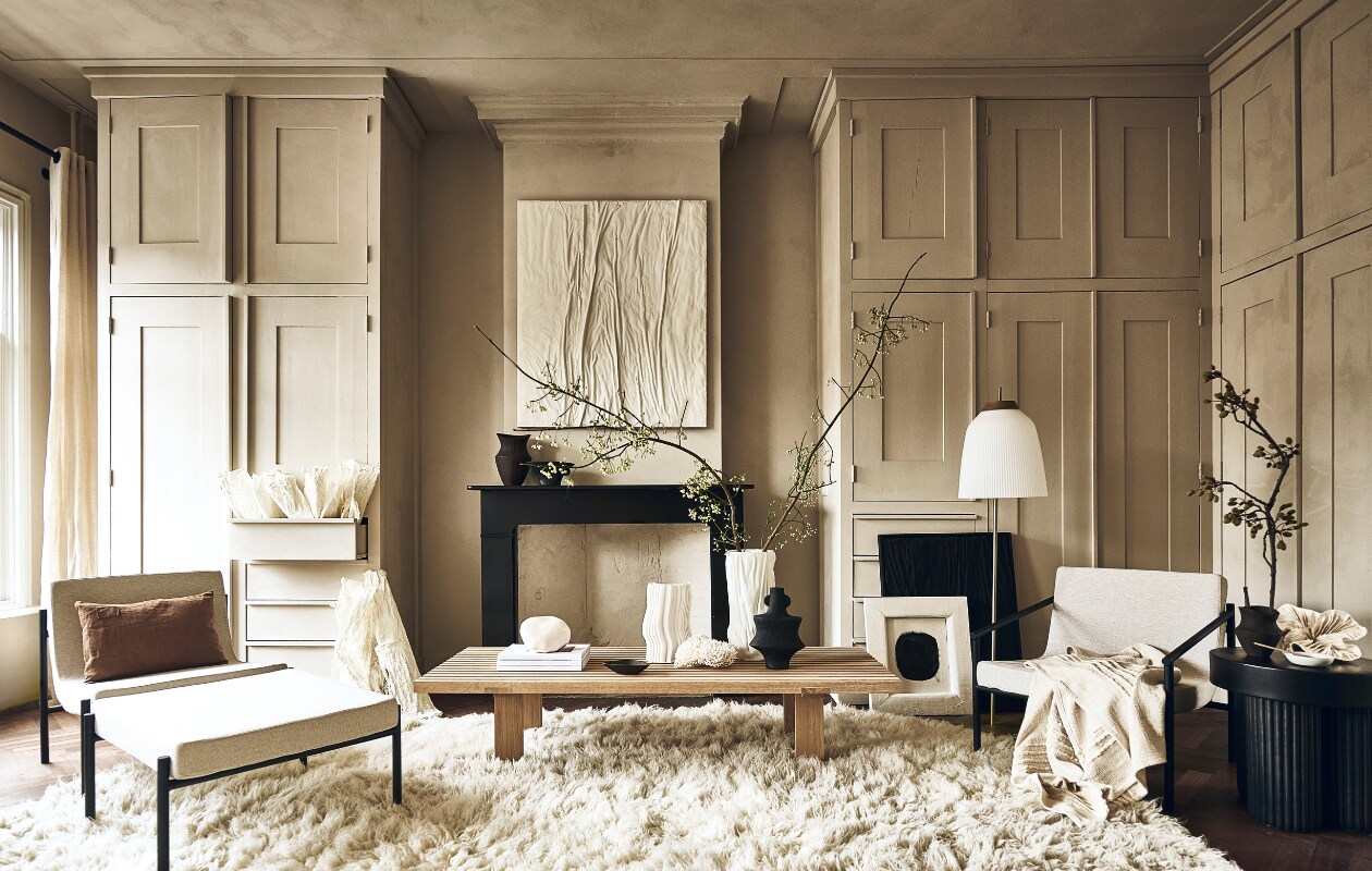 Crèmekleurige fauteuil Curve van Serax € 998,-, crèmekleurige fauteuil Curve van Serax met armleuningen € 1055,-, hocker Curve van Serax € 504,- (shop.vtwonen.be). Bruin kussen € 69,-, houten lepel op zwarte tafel € 24,50, witte schotel op zwarte tafel € 22,50 (sukha.nl). Papieren kunst tegen kast € 125,-, moerbeipapieren kunst op zwarte tafel € 795,- (elsavisser.com). Bruine vaas op schouw € 39,99, bruin schoteltje op salontafel € 17,99, bruine vaas op zwarte tafel € 22,99 (zarahome.com). Wit kunstwerk, 100×120 cm, prijs op aanvraag, zwart kunstwerk Water &amp; Cracked Mud, 60×80 cm € 990,-, witte vaas op salontafel Vase Sculpture Small € 480,- (studio-harte.com). Zwart bakje op schouw € 19,99, zwarte vaas op salontafel € 24,99 (hm.com). Witte siervorm op tafel € 295,- (taxidermy). Witte vaas links op tafel € 135,-, (fermliving.com). Stenen witte bol, prijs op aanvraag, houten salontafel vanaf € 1449,- (studiohenk). Wit vloerkleed, 235×350 cm € 1395,-, wit plaid € 99,- (eijerkamp). Vloerlamp vanaf € 840,- (bolia.com). Zwarte tafel € 449,-, boeken € 22,- (aedamanthony.nl). Wit kunstwerk met zwarte ronding, prijs op aanvraag (@ansdekruyf). Muurkleur en vloer onbekend. Overig privébezit.