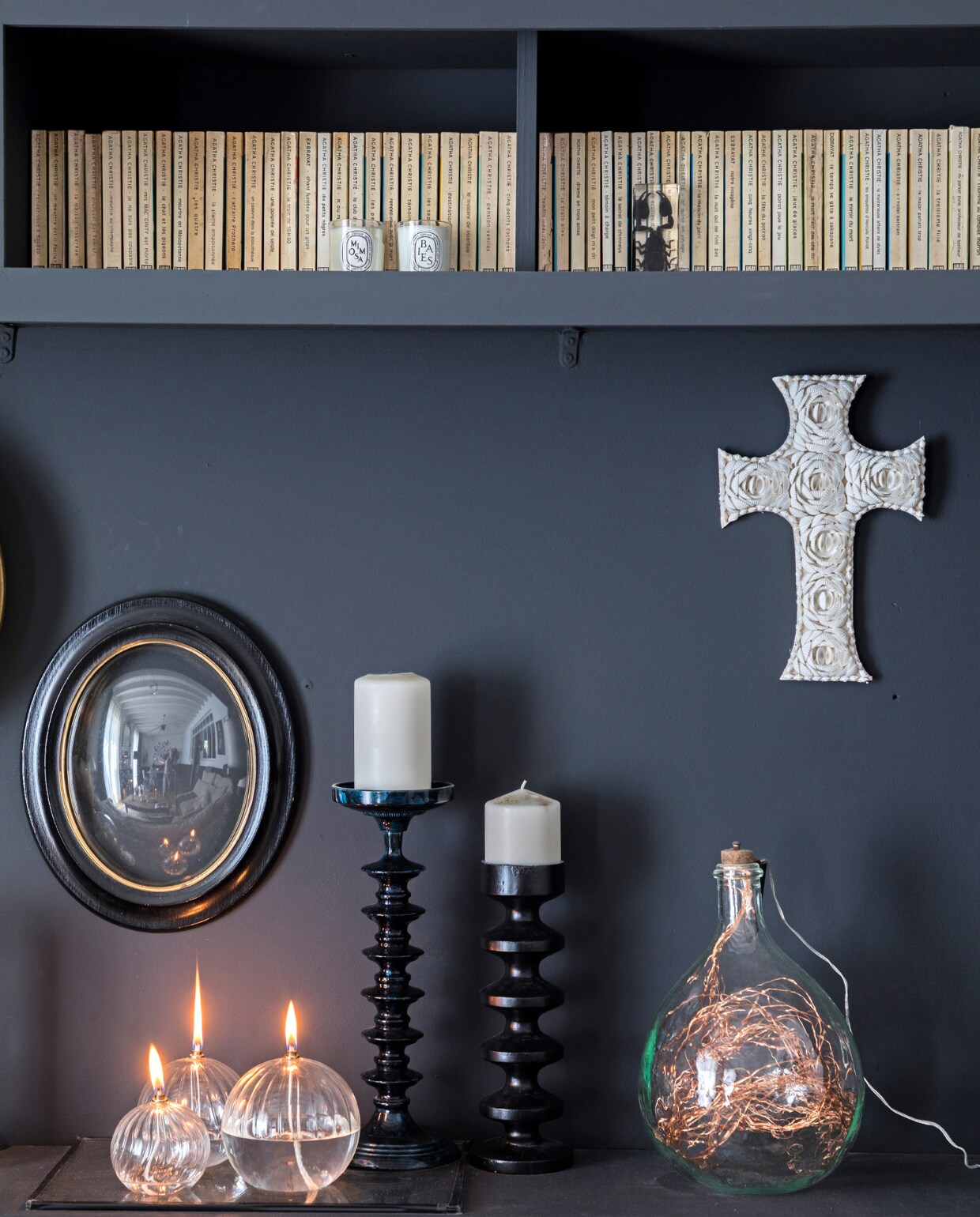 Boekenkast geverfd in Off-Black van Farrow &amp; Ball. Spiegel en kruis antiek, glazen fles vintage. Vergelijk- bare items: kandelaars BePureHome, set olielampen Bol, koperen lichtsnoer Hema.